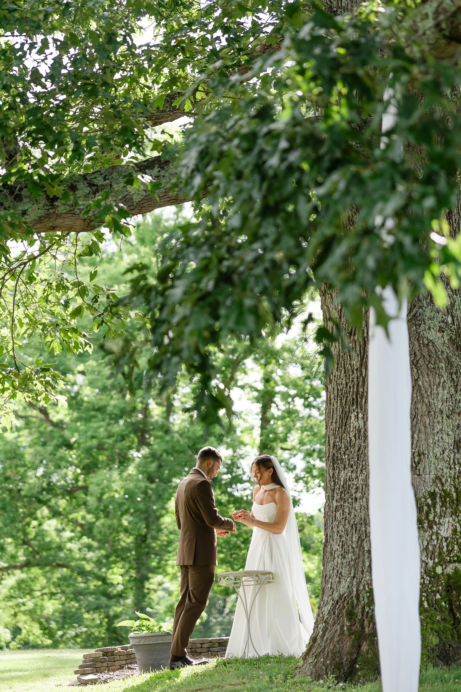 Bride and groom share private vows under a large oak tree in a lush green outdoor wedding setting.