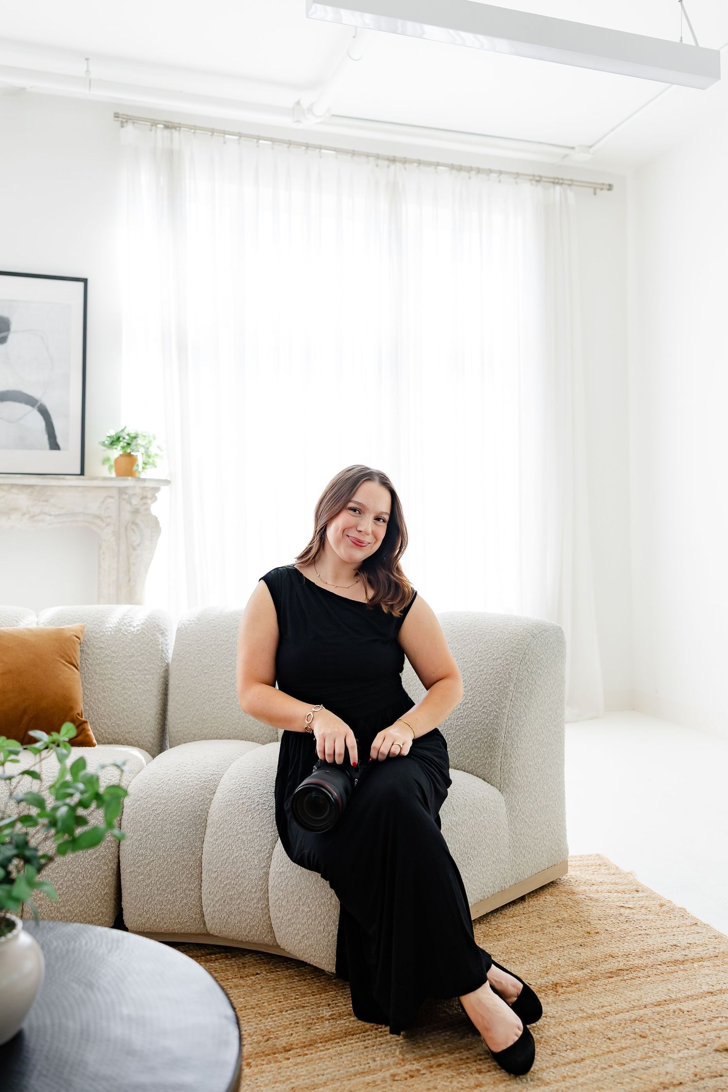 Woman in black jumpsuit sitting on a modern white boucle sofa in a bright, minimalist living room.
