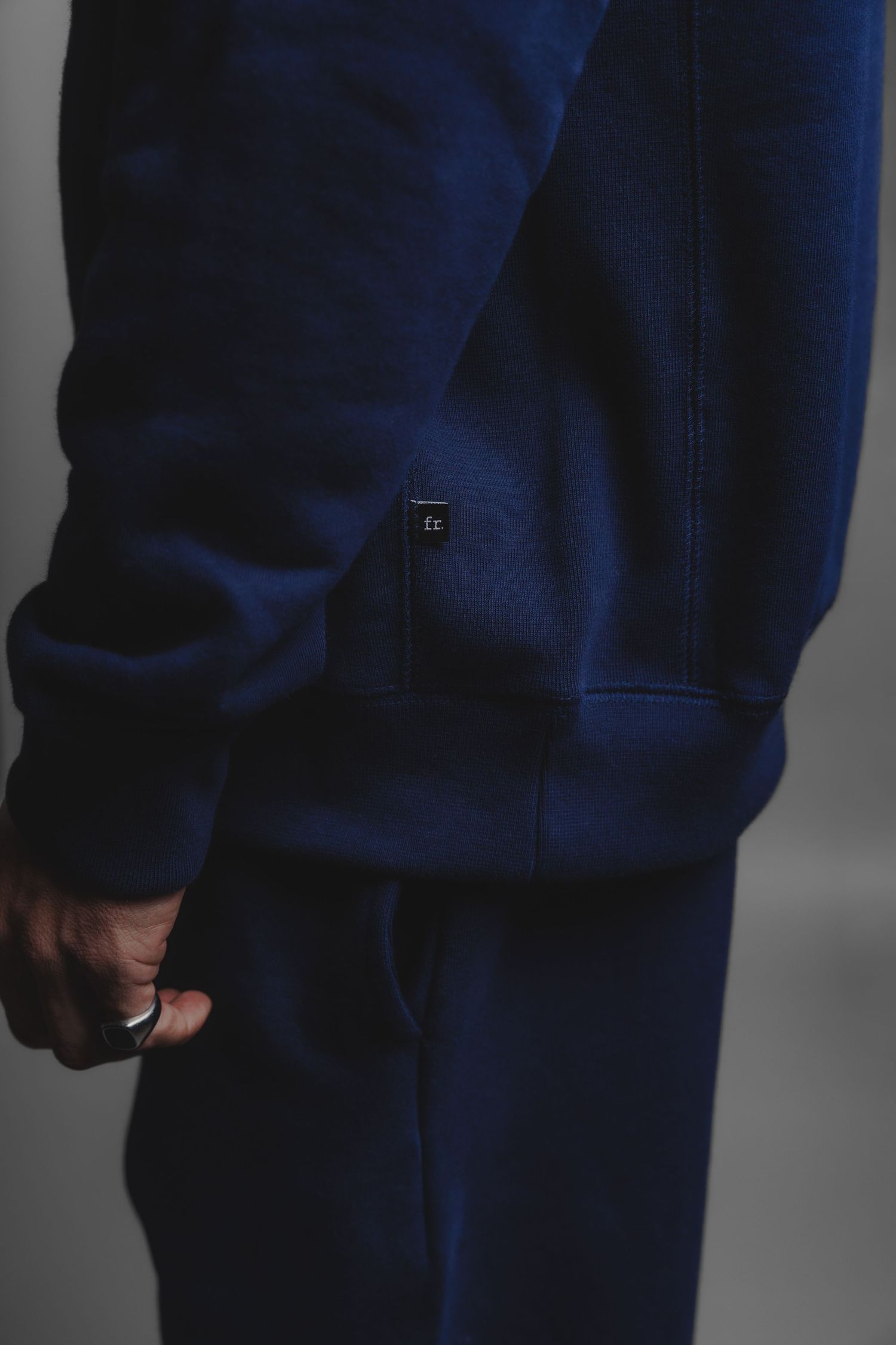 Close-up detail of navy blue hoodie sleeve with small logo tag and matching sweatpants.
