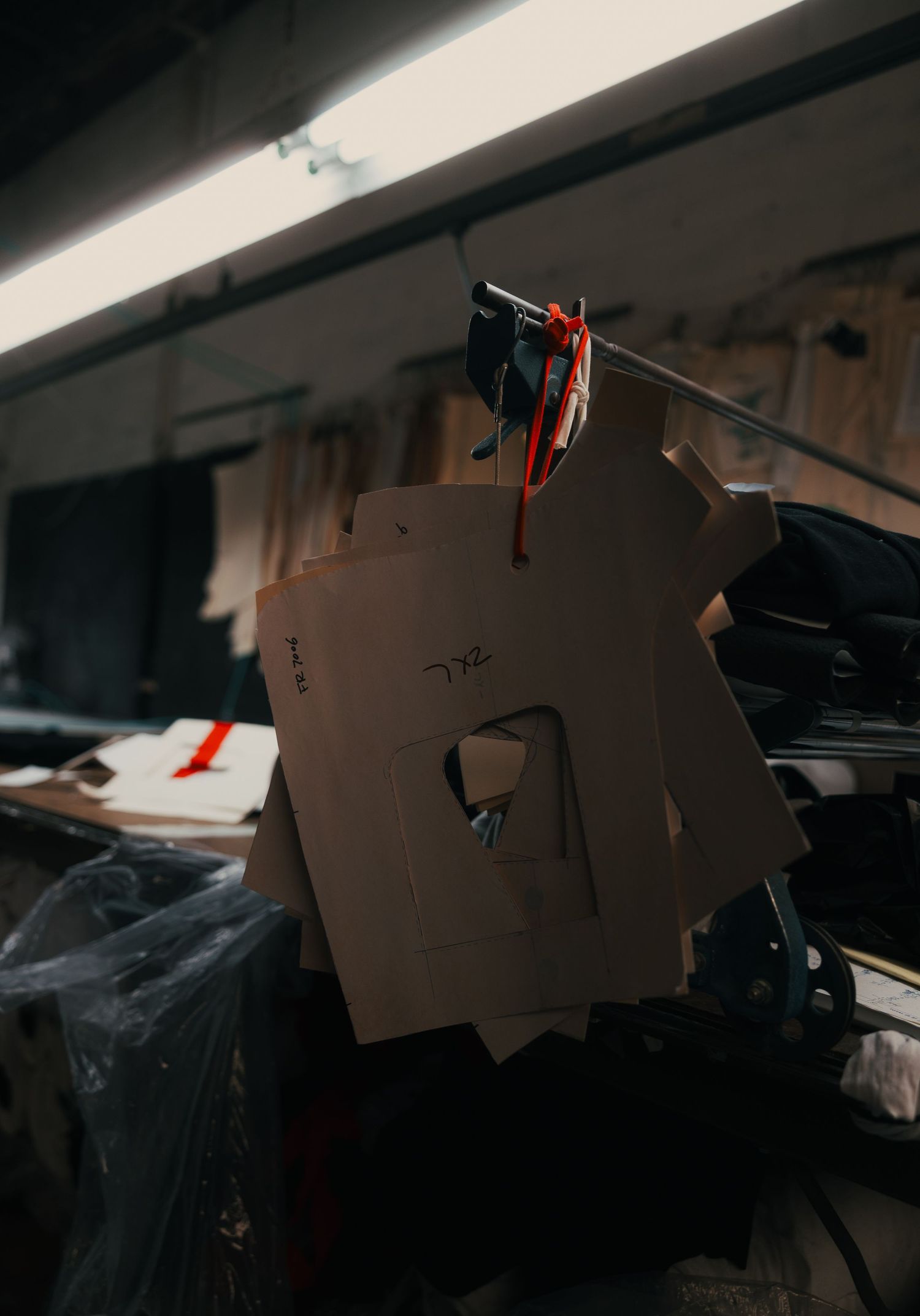 Cardboard pattern templates hanging on a wire in a cluttered garment manufacturing workspace.