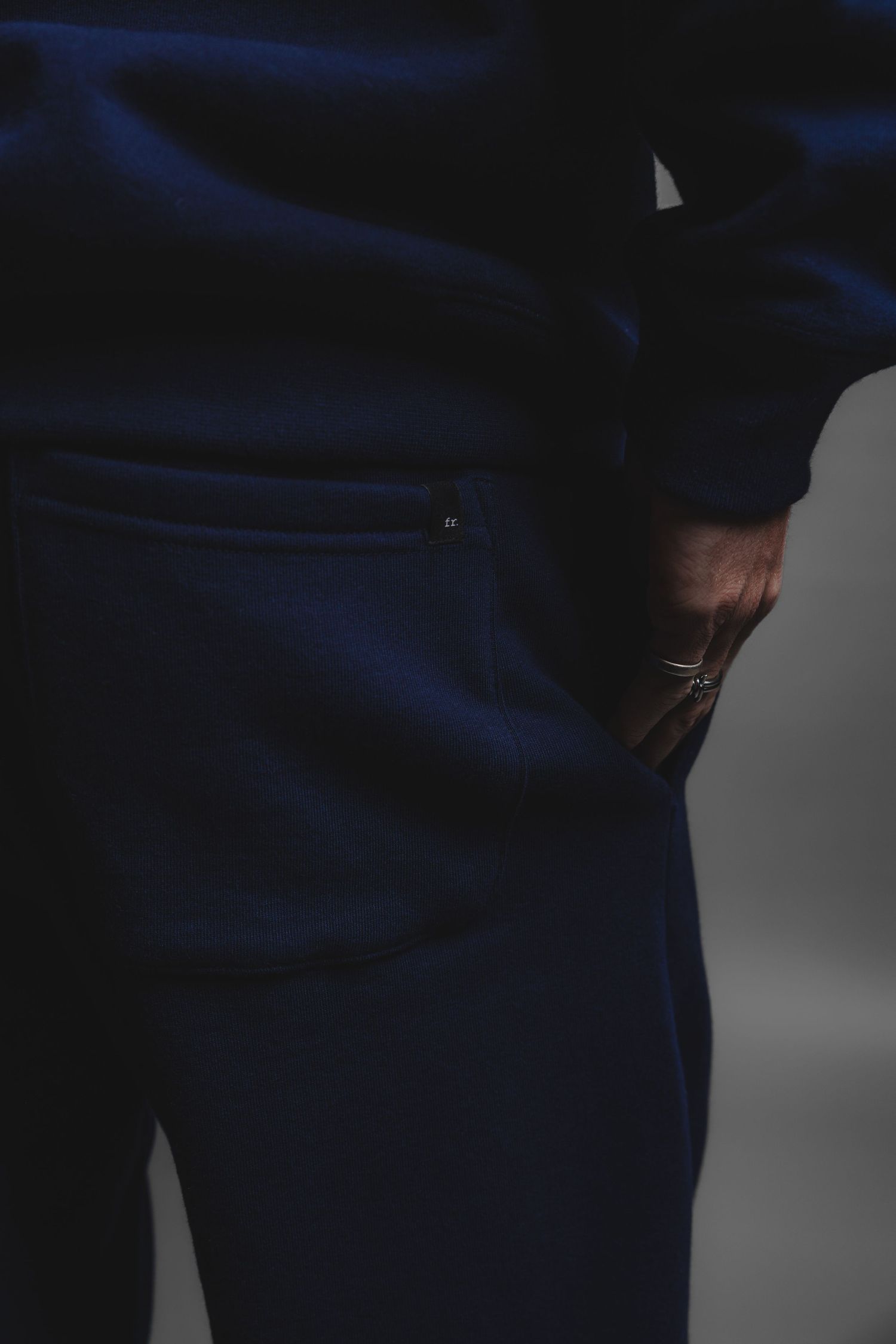 Close-up back view of navy blue jogger pants with a zip pocket and a hand showing a ring.