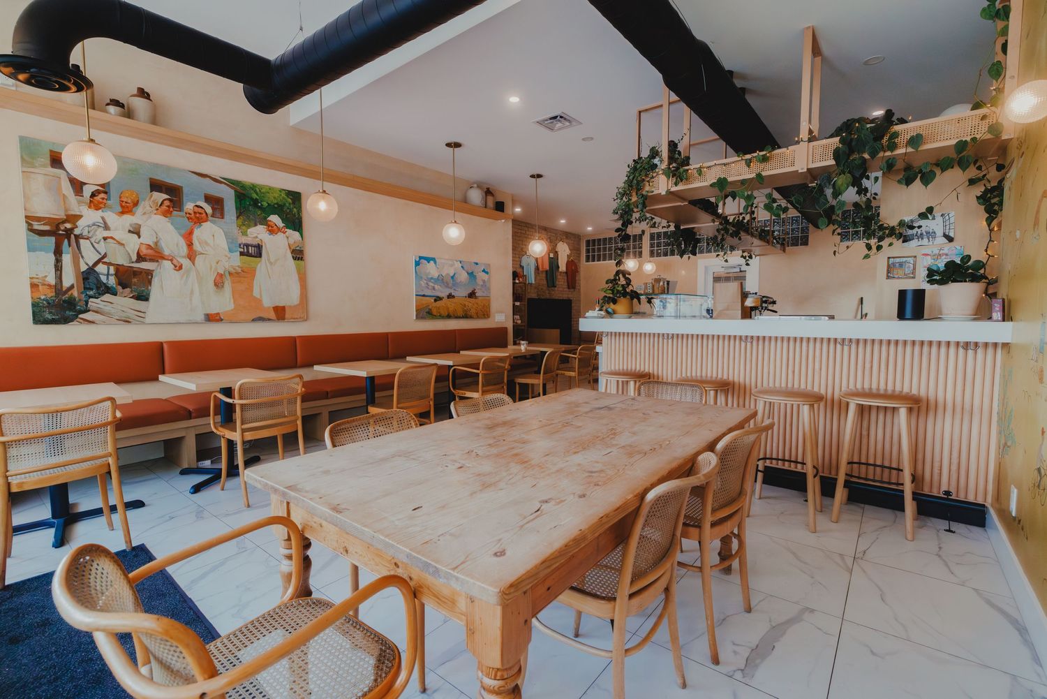 Bright cafe interior with wooden tables, rattan chairs, green plants, and colorful wall art in a modern restaurant.