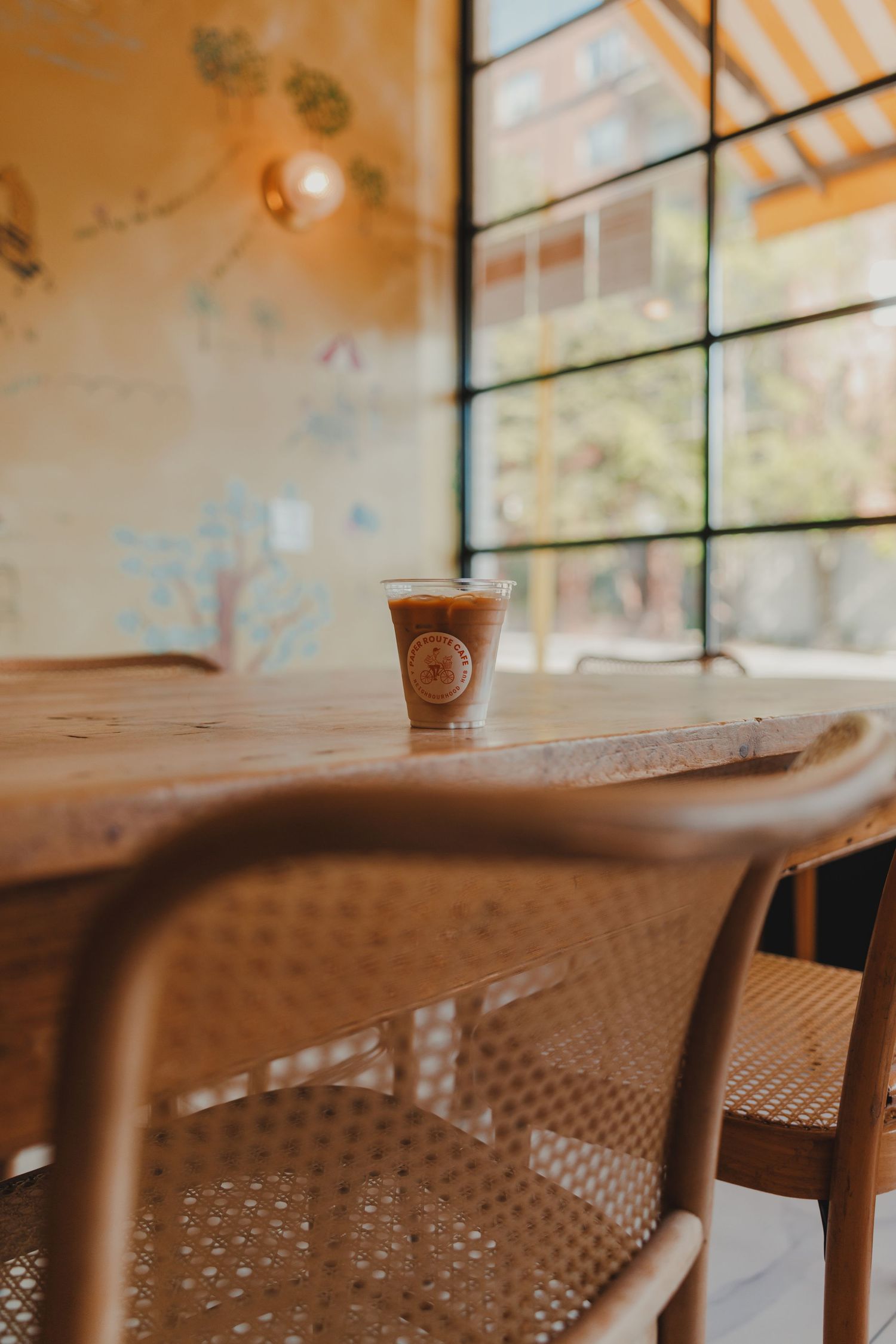 Iced coffee drink in a branded cup on a rustic wooden table by large windows in a warm café.