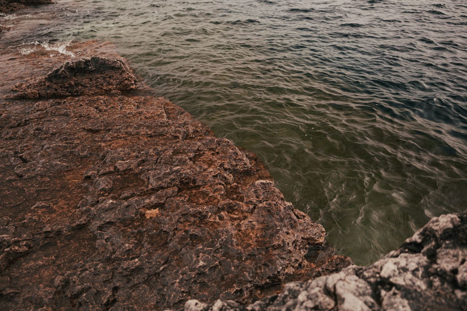 Rocky coastal shoreline with dark stones meeting choppy ocean waters under an overcast sky.