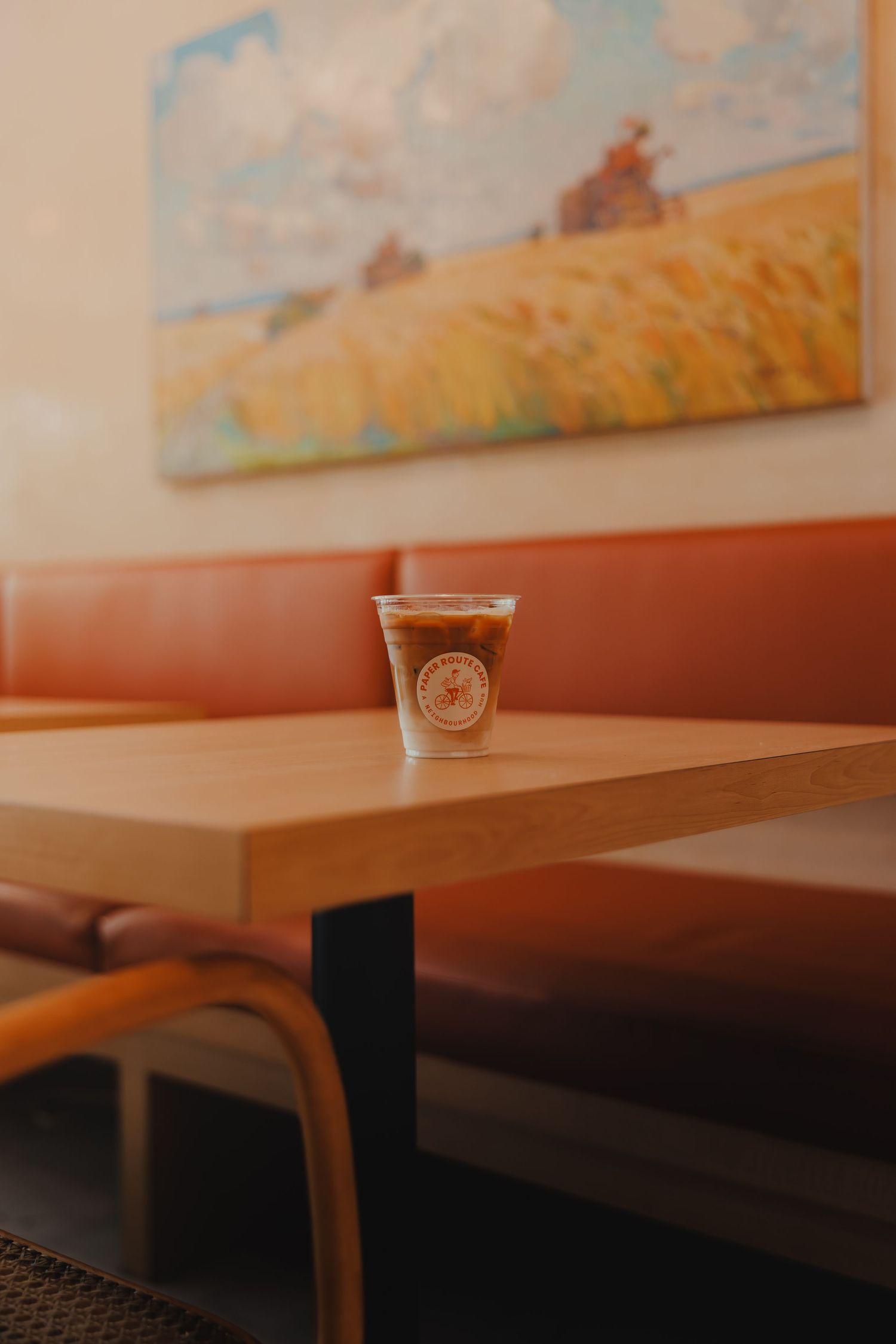 Branded iced coffee cup sitting alone on wooden table in cozy cafe booth seating.