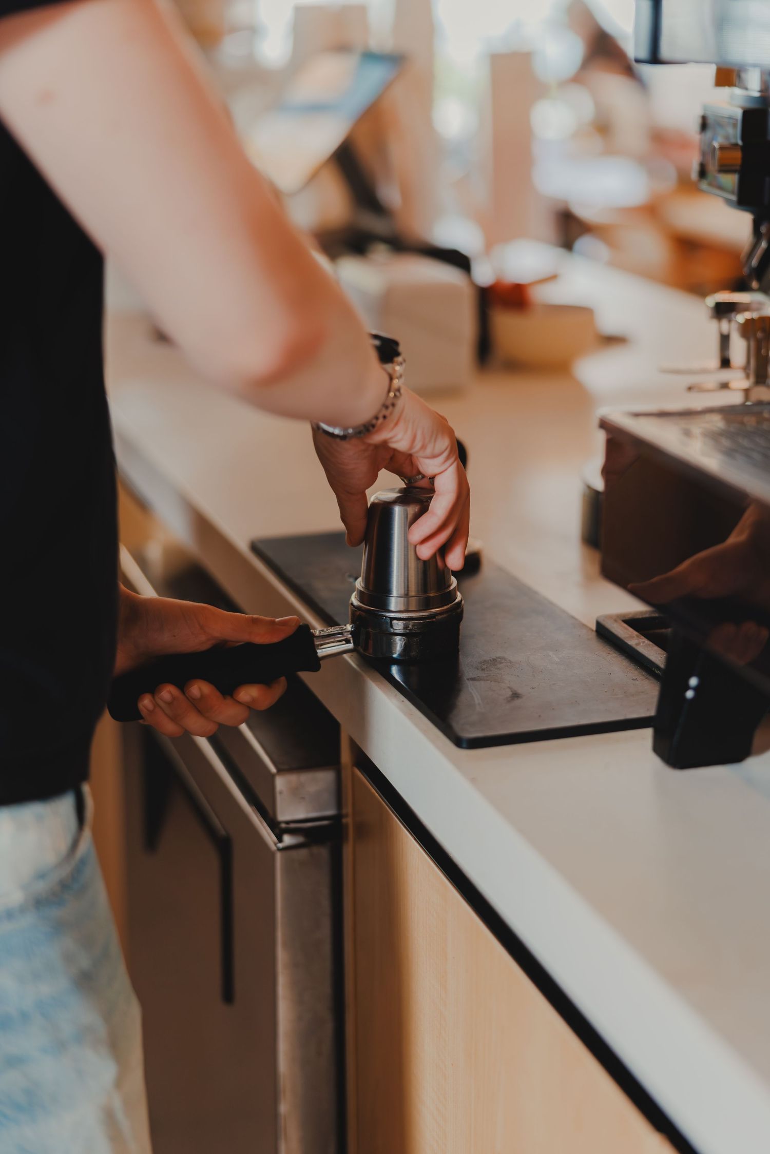 Barista tamping espresso grounds in portafilter on a cafe counter.