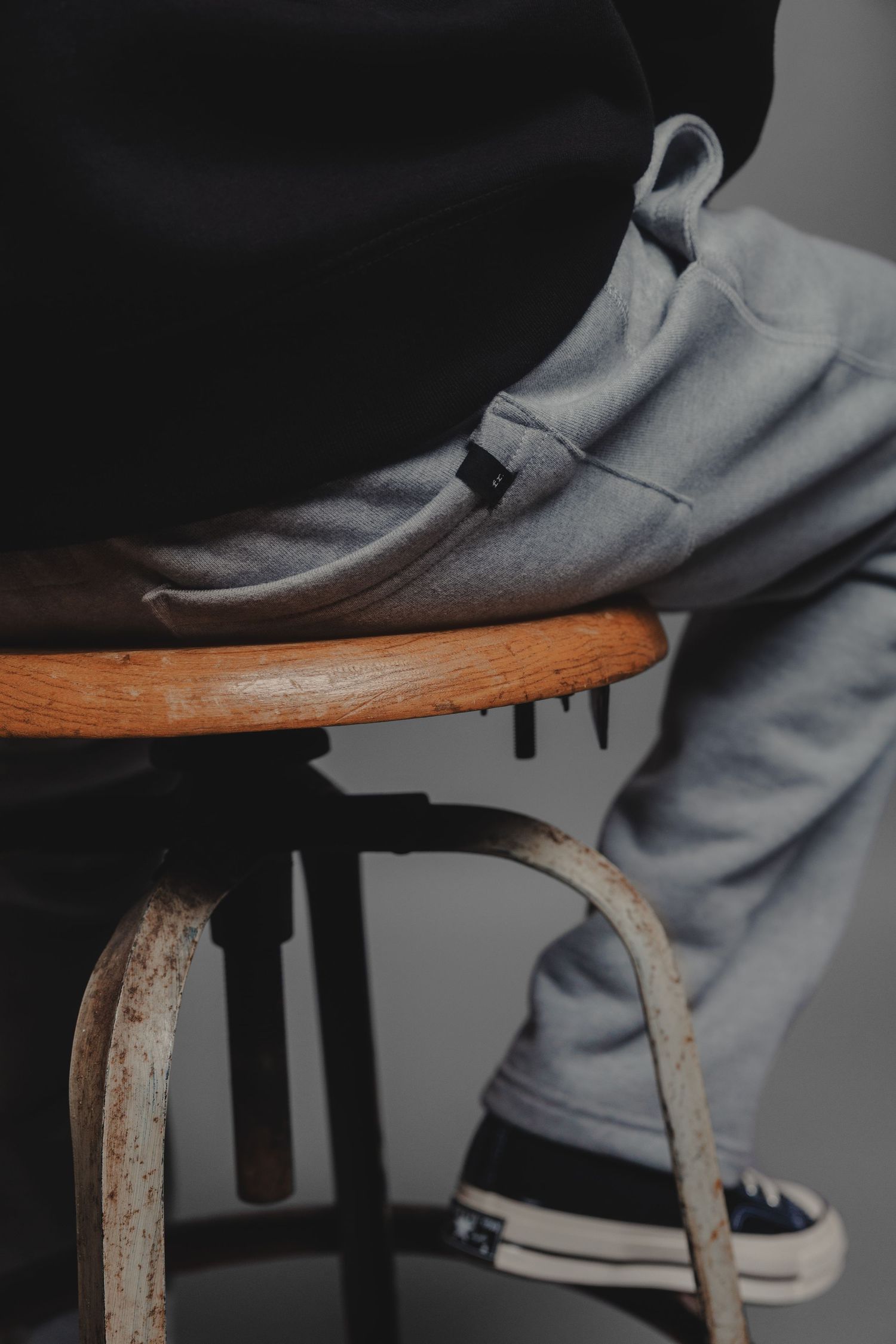 Person sitting on vintage stool wearing grey sweatpants and black Converse sneakers.