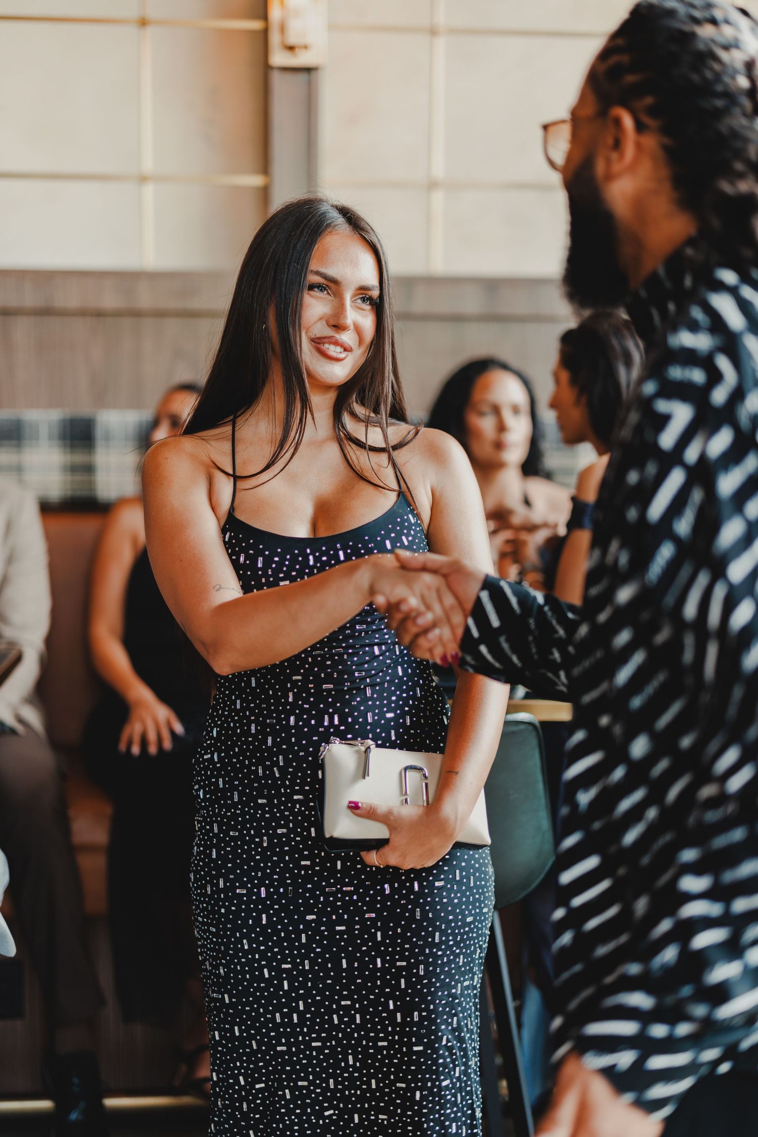 Woman in navy polka dot dress smiling and shaking hands at a formal event.