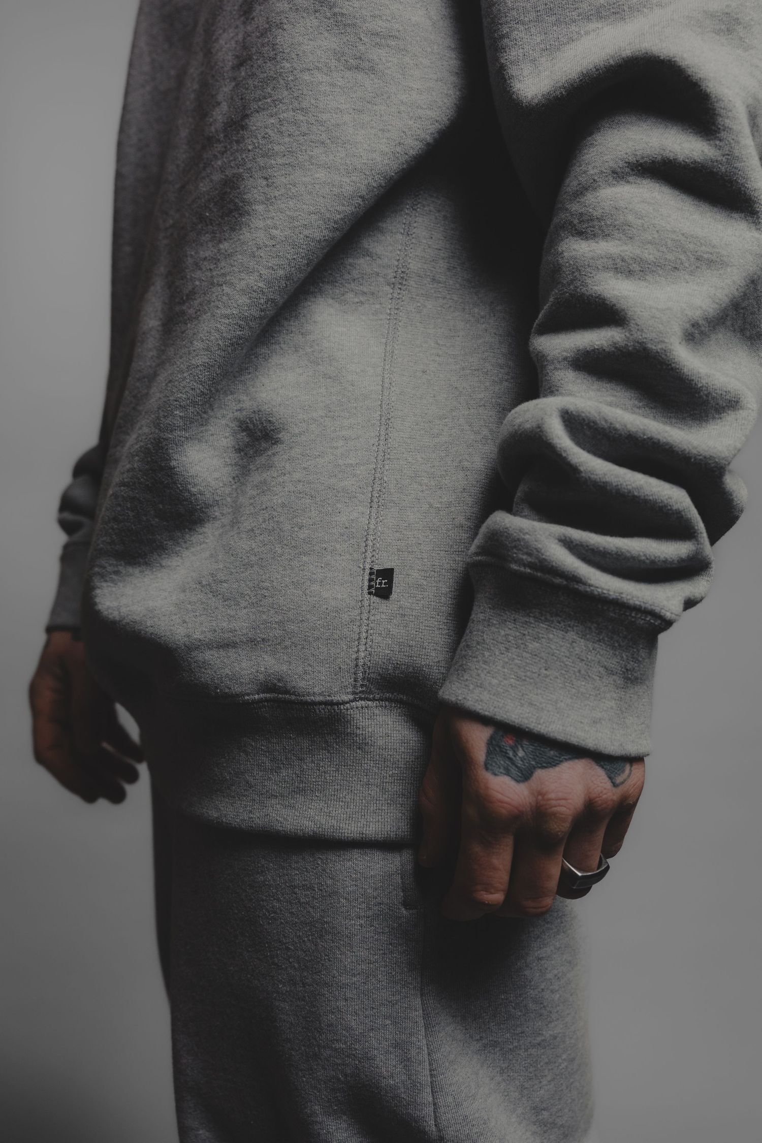 Close-up of gray fleece sweatsuit with tattooed hand visible at cuff on gray background.