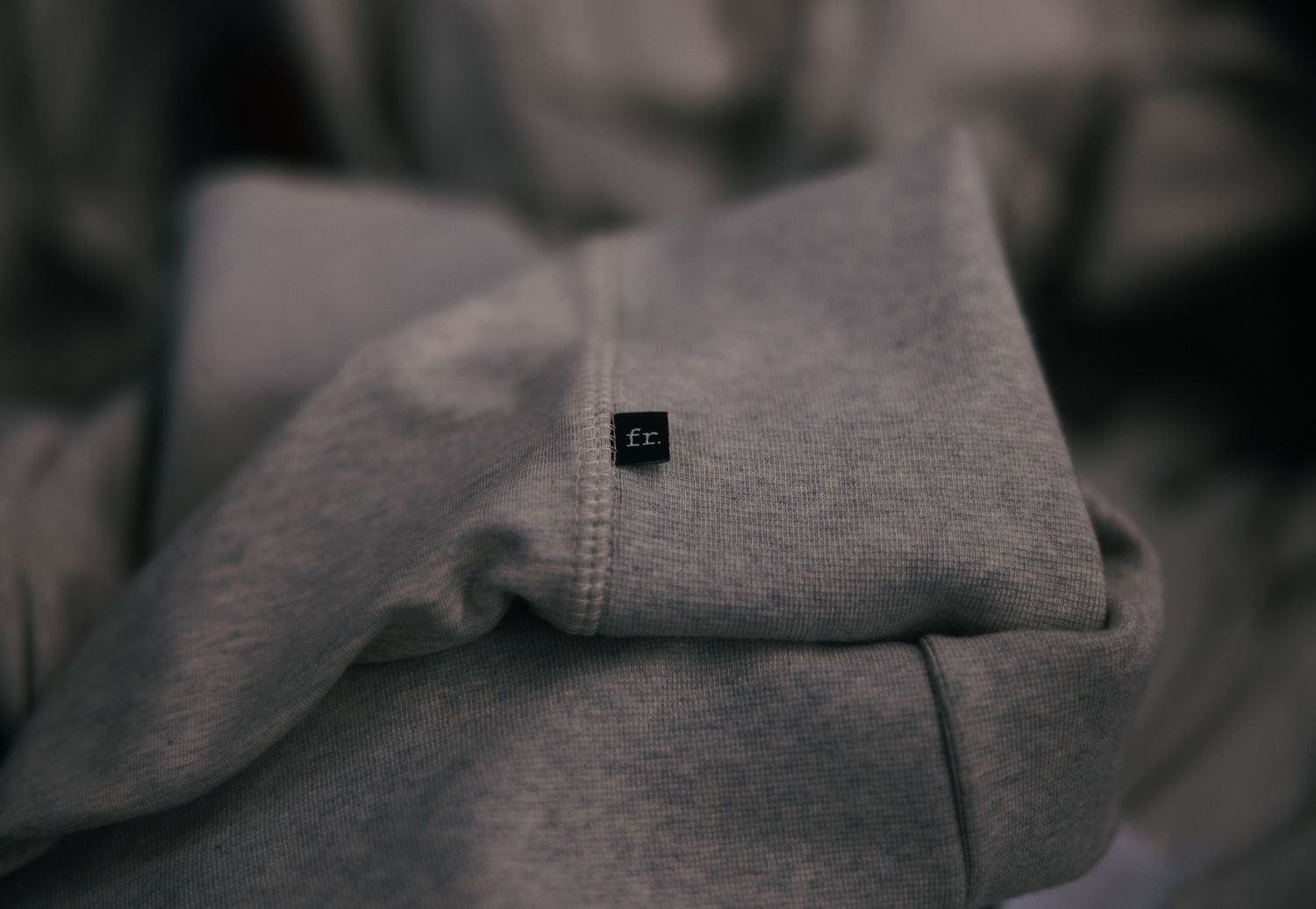 Close-up of a gray heathered hoodie with a small black ZC logo patch on the sleeve.