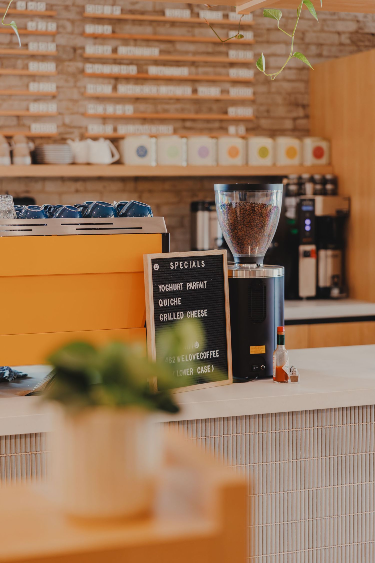 Cozy cafe counter with coffee grinder, specials chalkboard menu, and warm wood decor in a modern coffee shop.