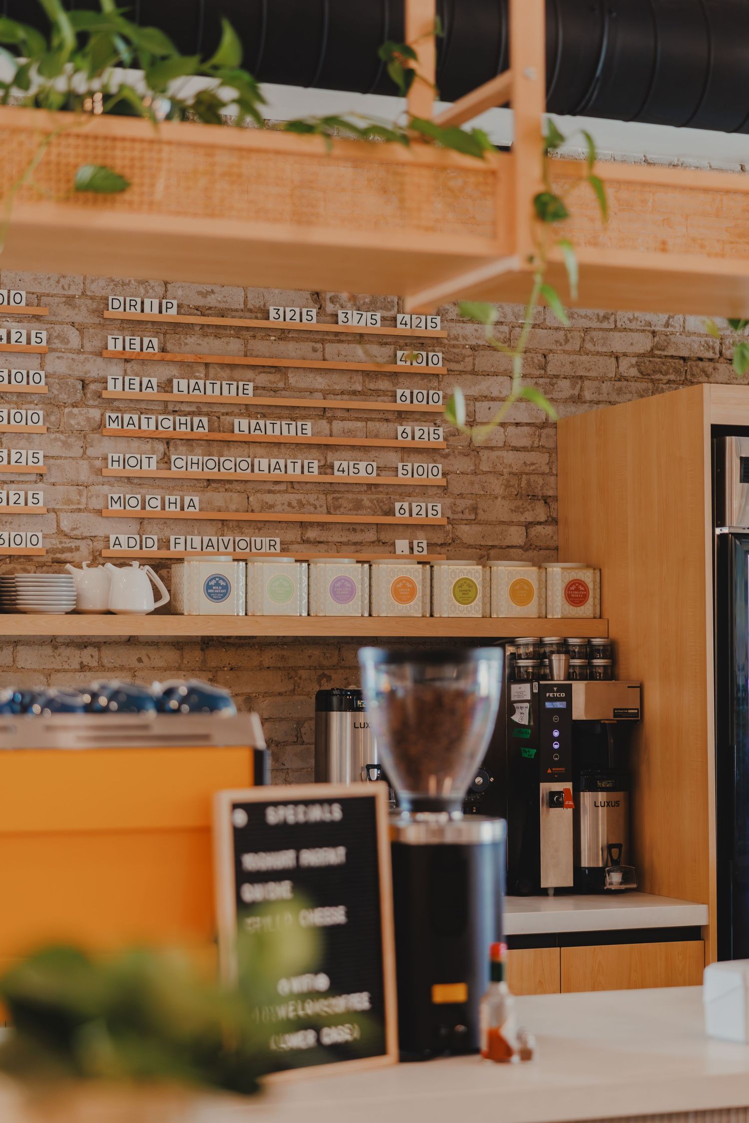Cozy cafe interior with brick wall menu board, coffee grinder, and specials chalkboard sign.