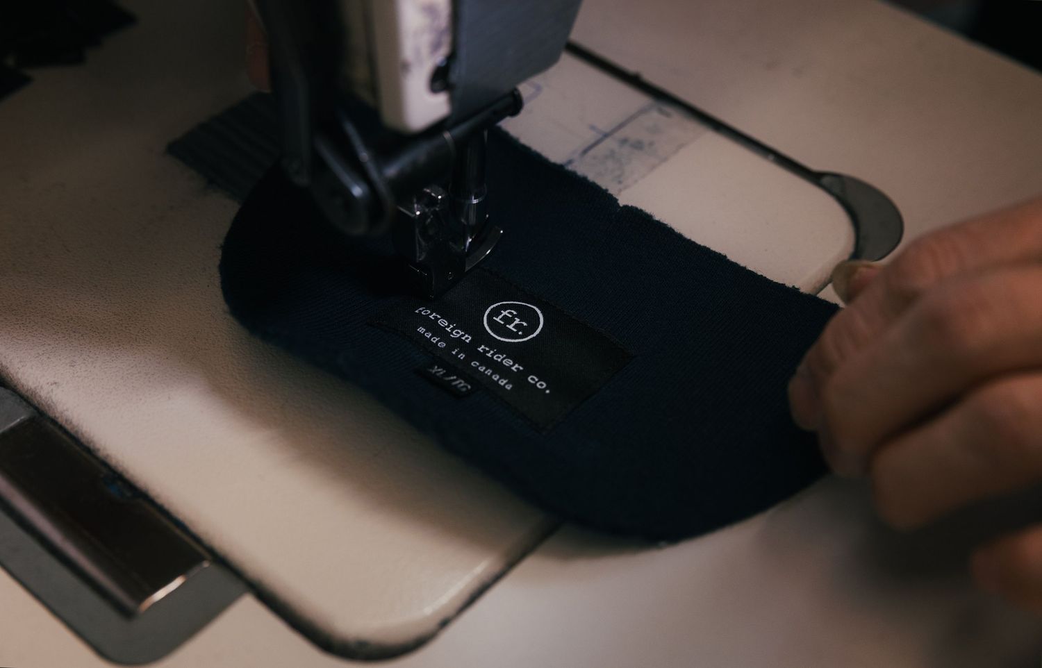 Close-up of a sewing machine stitching a dark fabric label with white text in a garment factory.