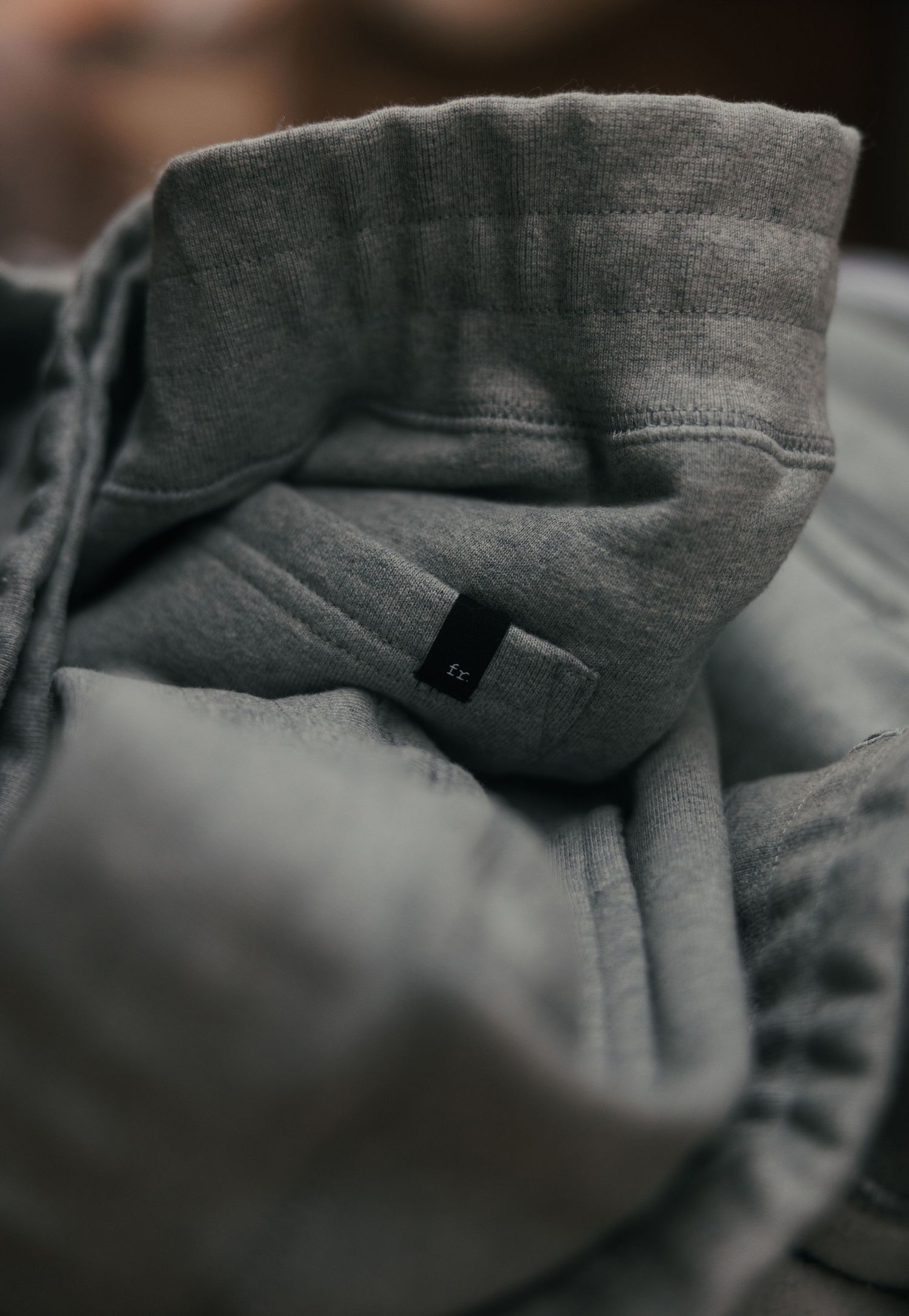 Close-up of a folded gray hoodie sweatshirt with a small black label tag visible on the inner collar.