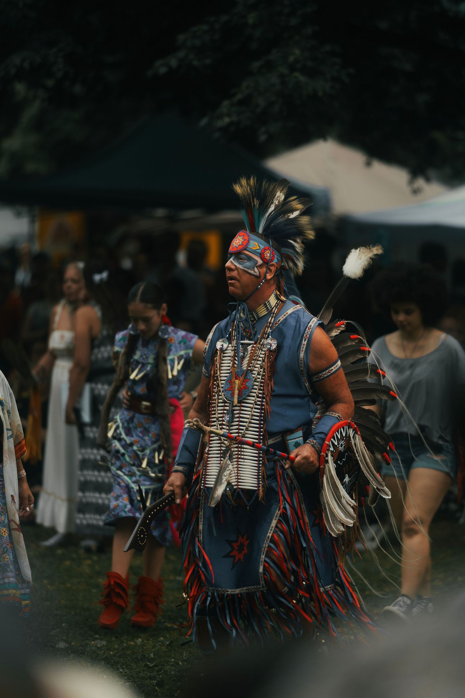 Native American dancer in traditional regalia with feathered headdress performs at an outdoor powwow cultural event.
