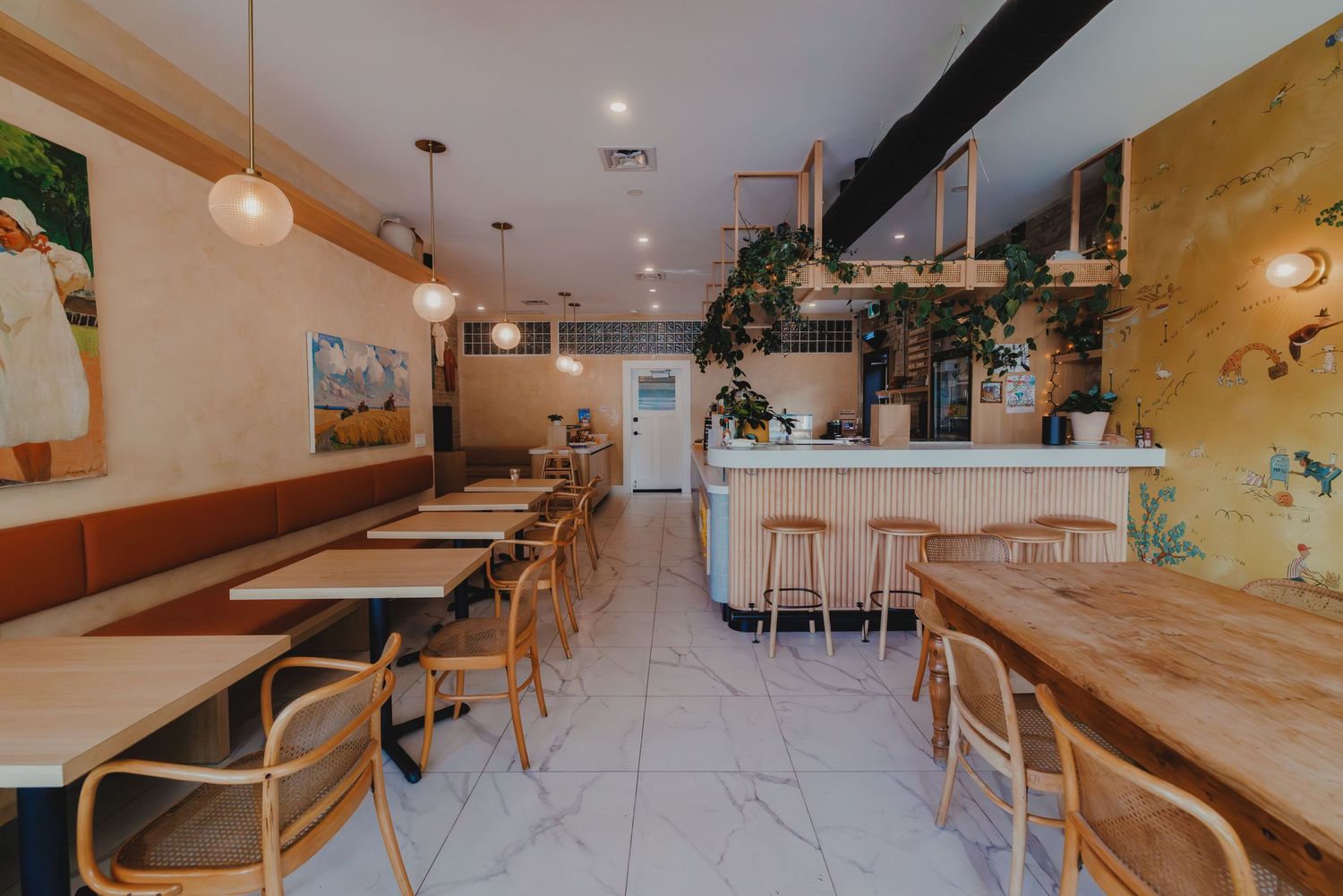 Bright and airy cafe interior with marble floors, rattan chairs, wooden tables, and lush hanging plants.