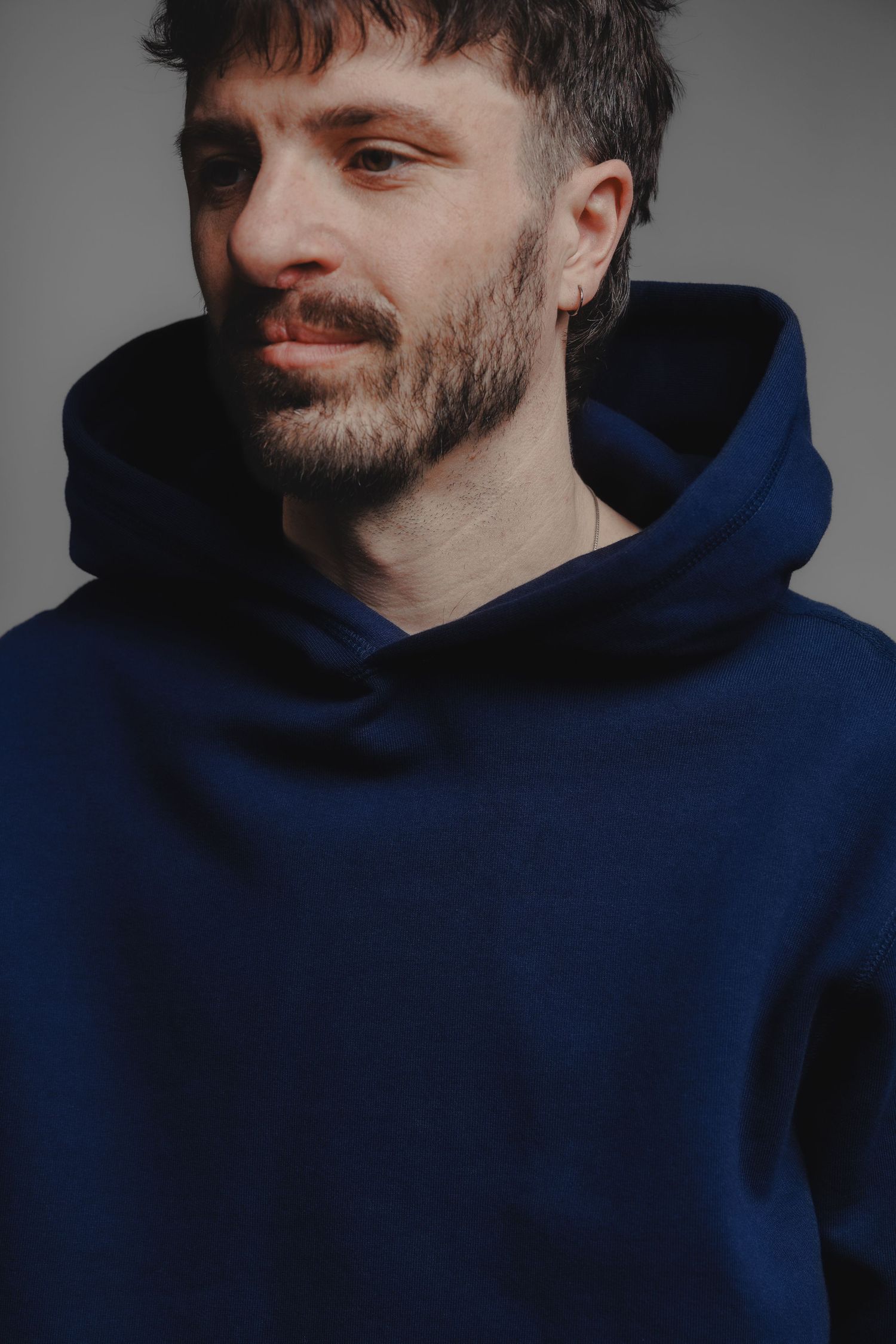 Man with beard wearing a navy blue oversized hoodie against a grey background.