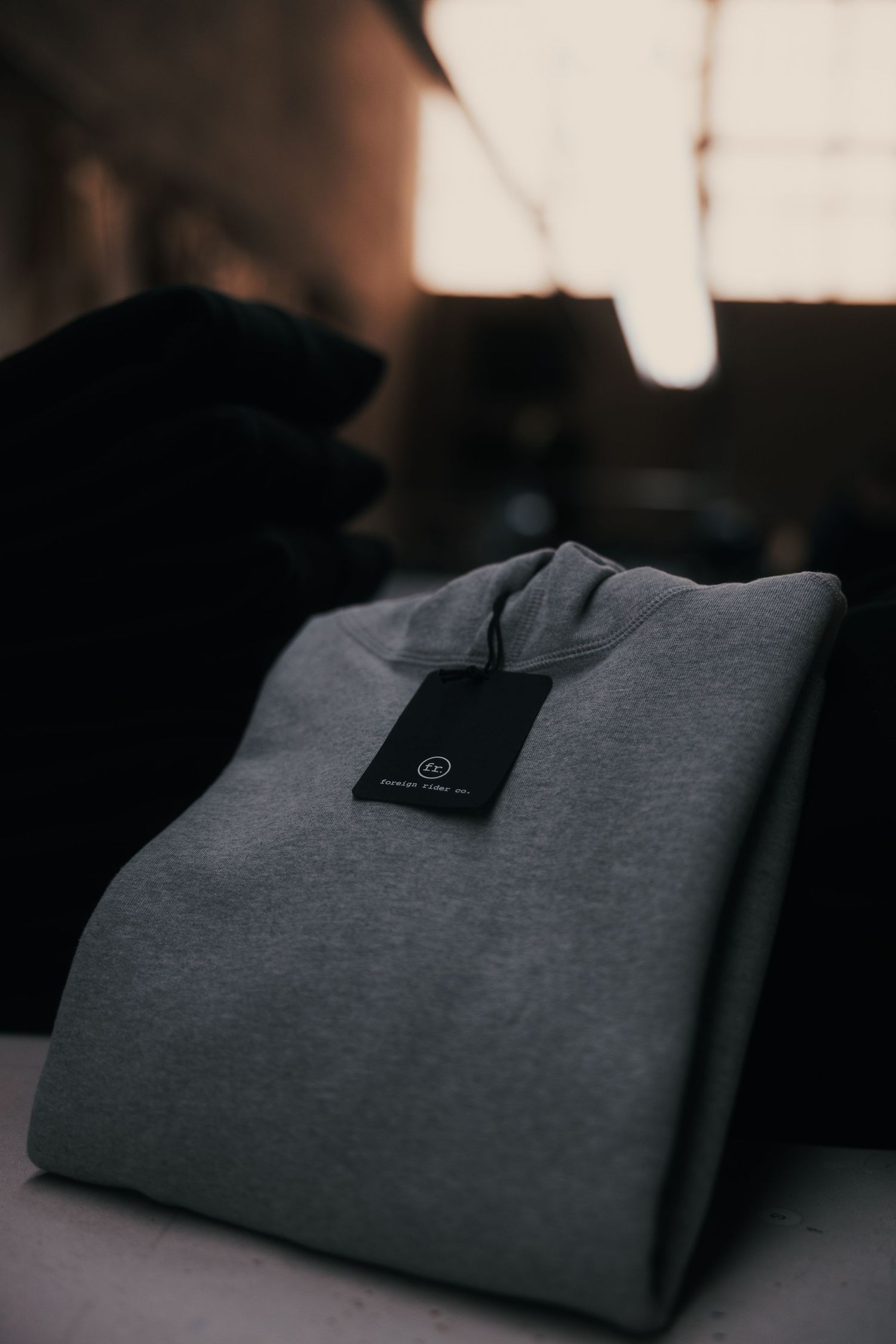 Folded gray sweatshirt with black hang tag on white surface in moody dark background.