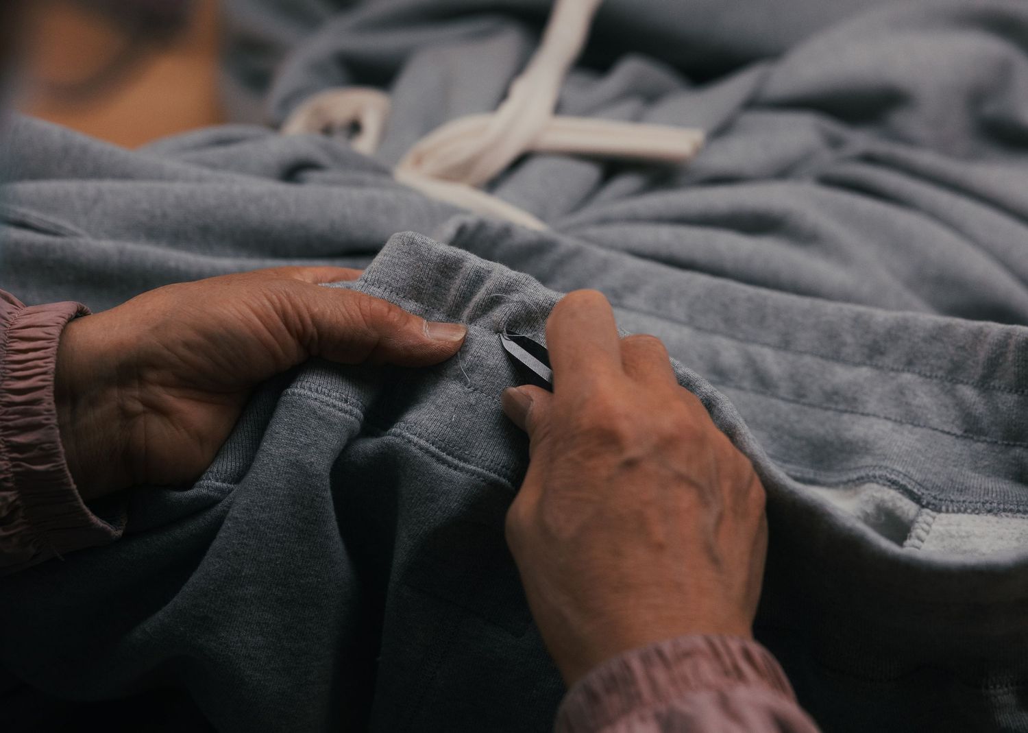 Elderly hands carefully fastening a snap button on a gray sweatshirt garment during clothing production.
