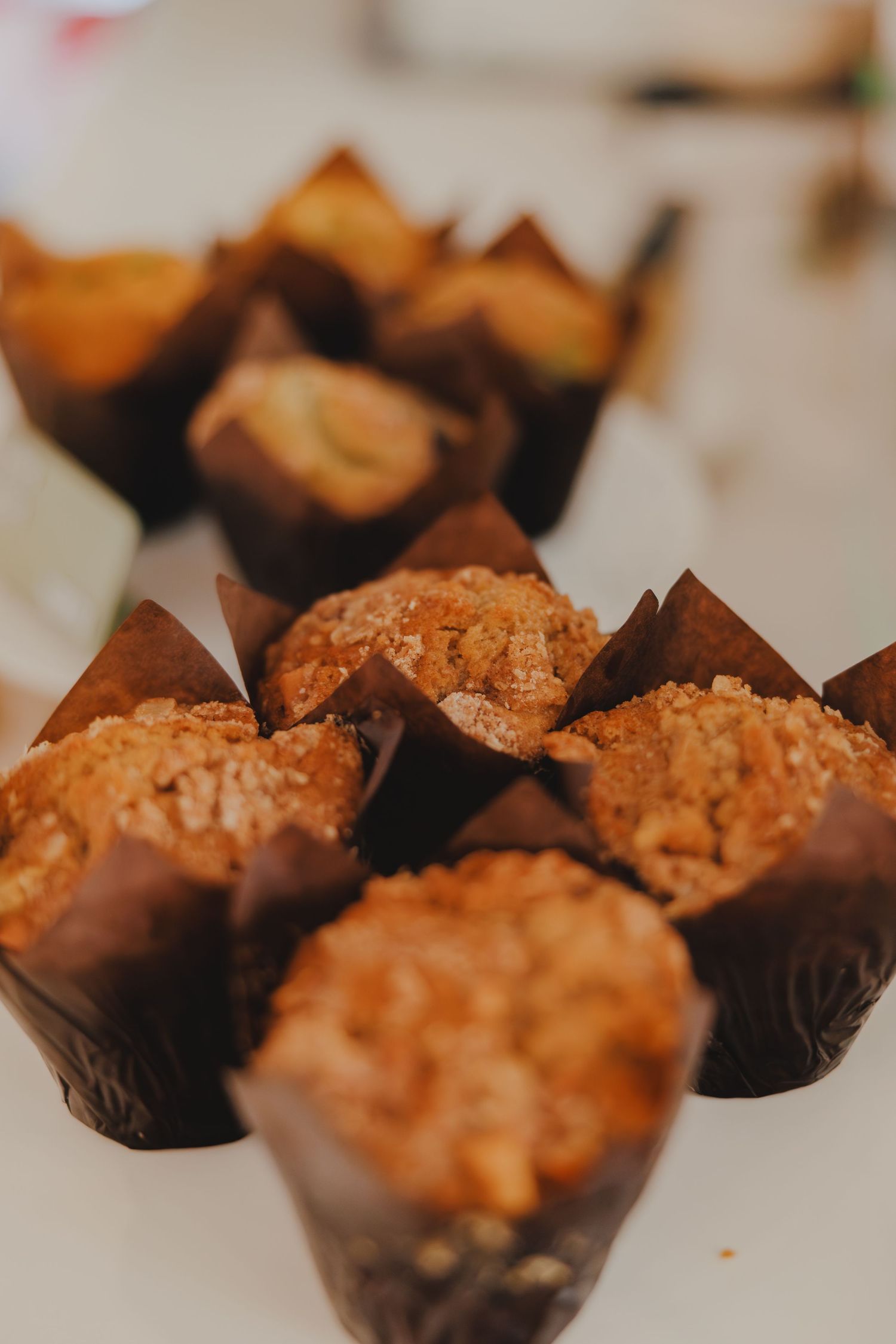 Freshly baked streusel muffins in brown tulip paper cups displayed on a white surface.