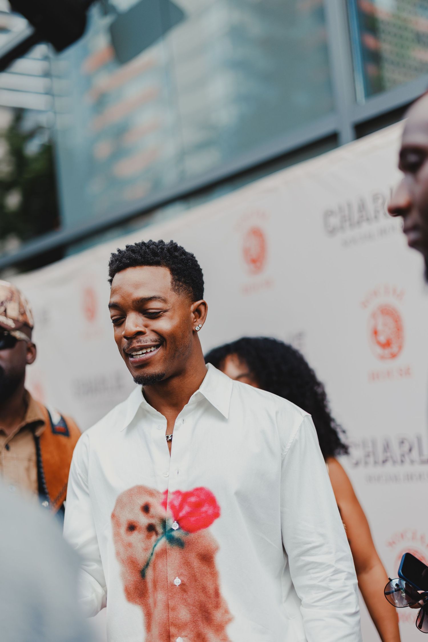 A smiling young man in a white shirt holds a red rose at a Charlie movie premiere red carpet event.