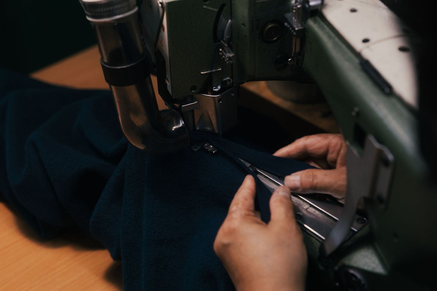 Close-up of hands guiding dark fabric through an industrial sewing machine in a professional tailor workshop.