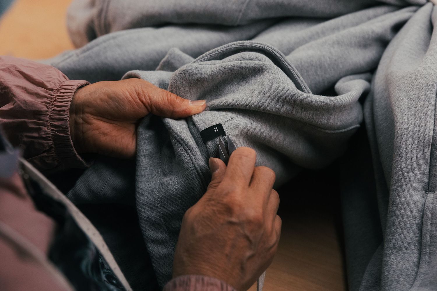 Close-up of hands zipping a gray hoodie sweatshirt pocket, showcasing fabric texture and zipper detail.