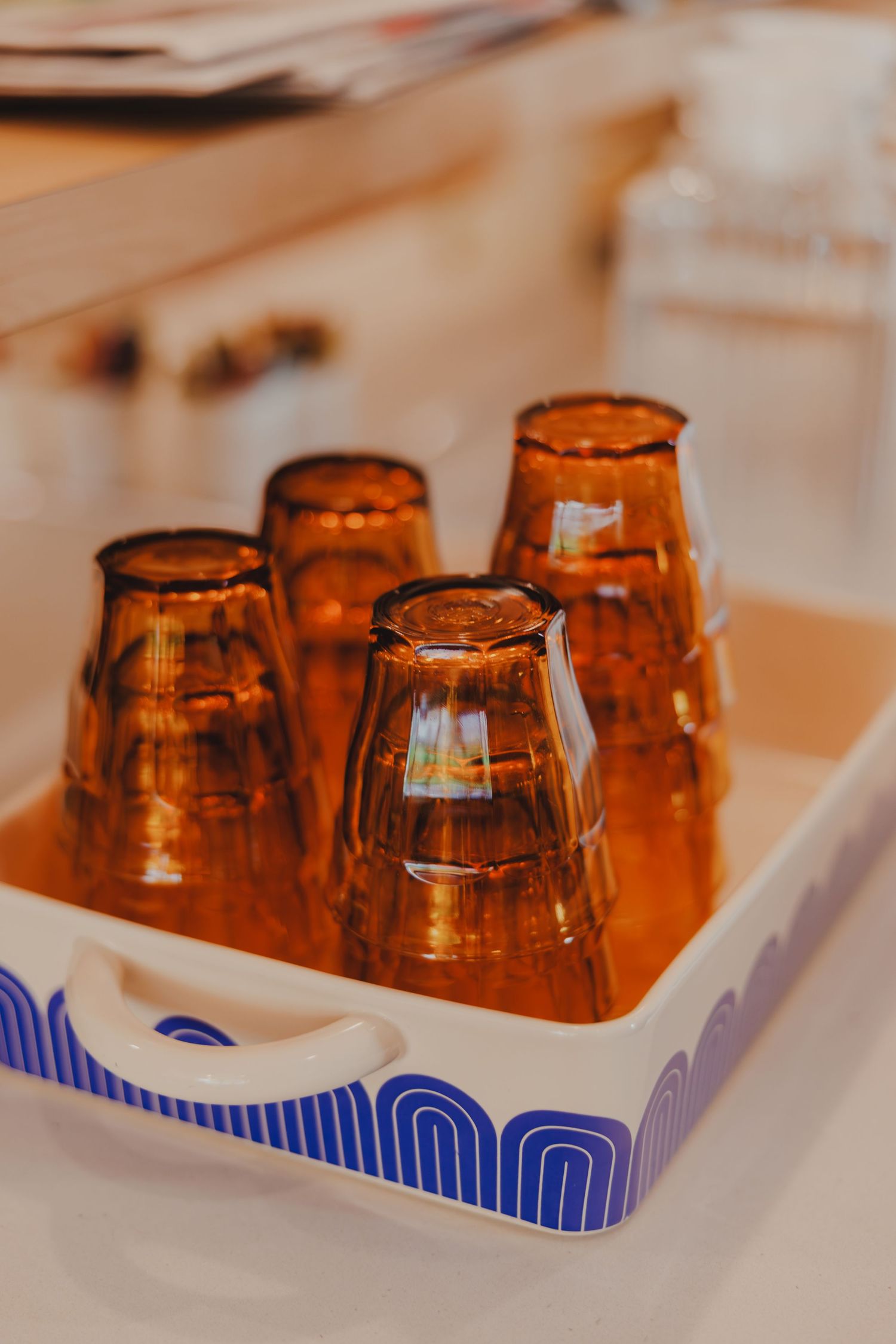 Four amber glass tumblers upside down on a decorative white tray with blue pattern.