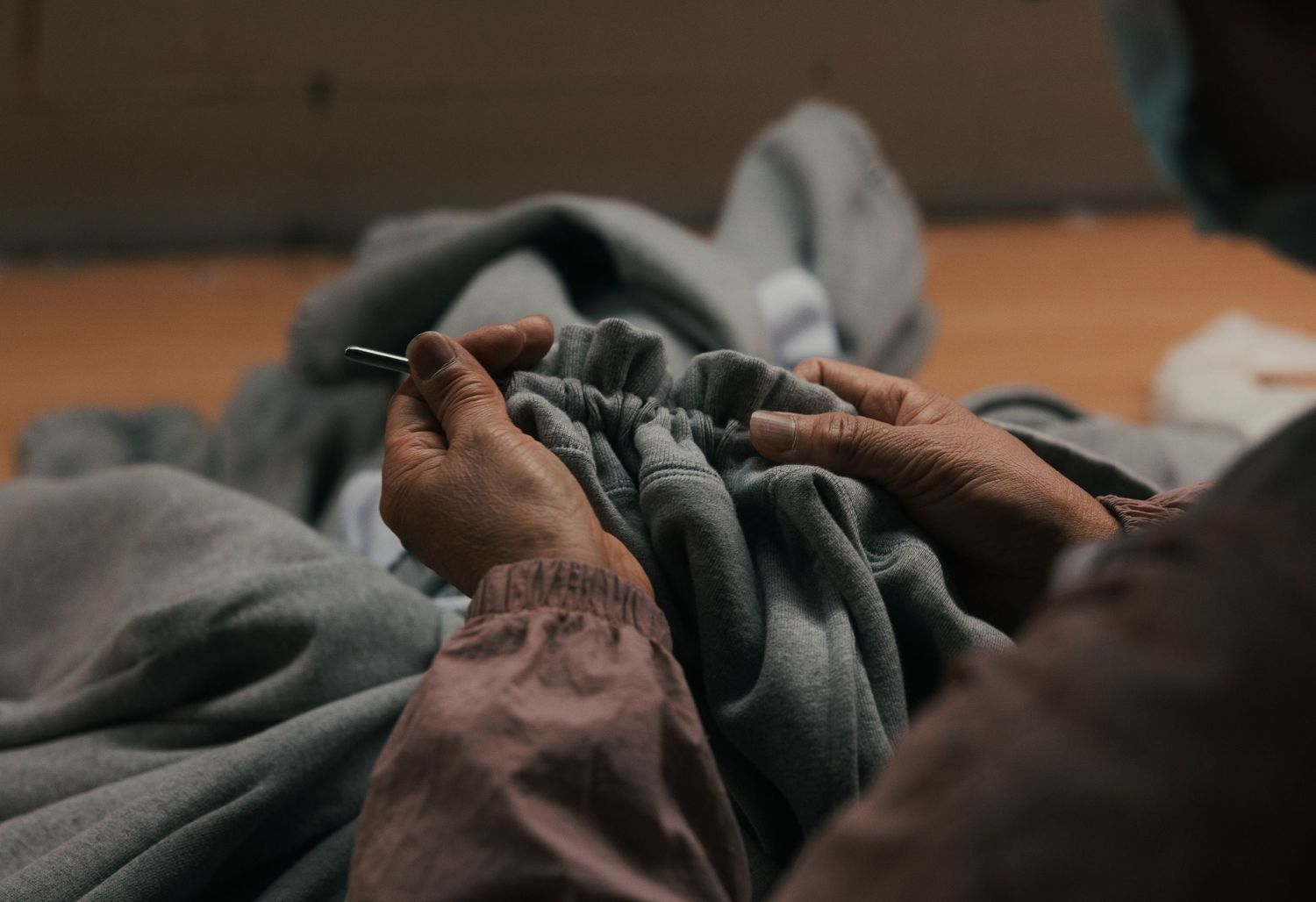 Hands carefully pinning gray fabric with a needle during garment sewing or tailoring work.