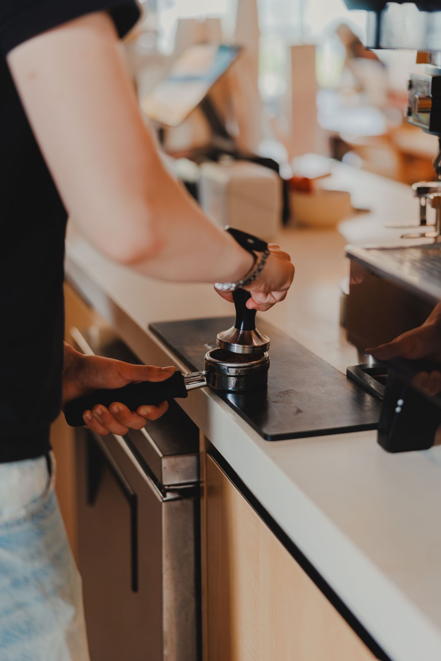 Barista tamping espresso grounds into portafilter on cafe counter during coffee preparation.