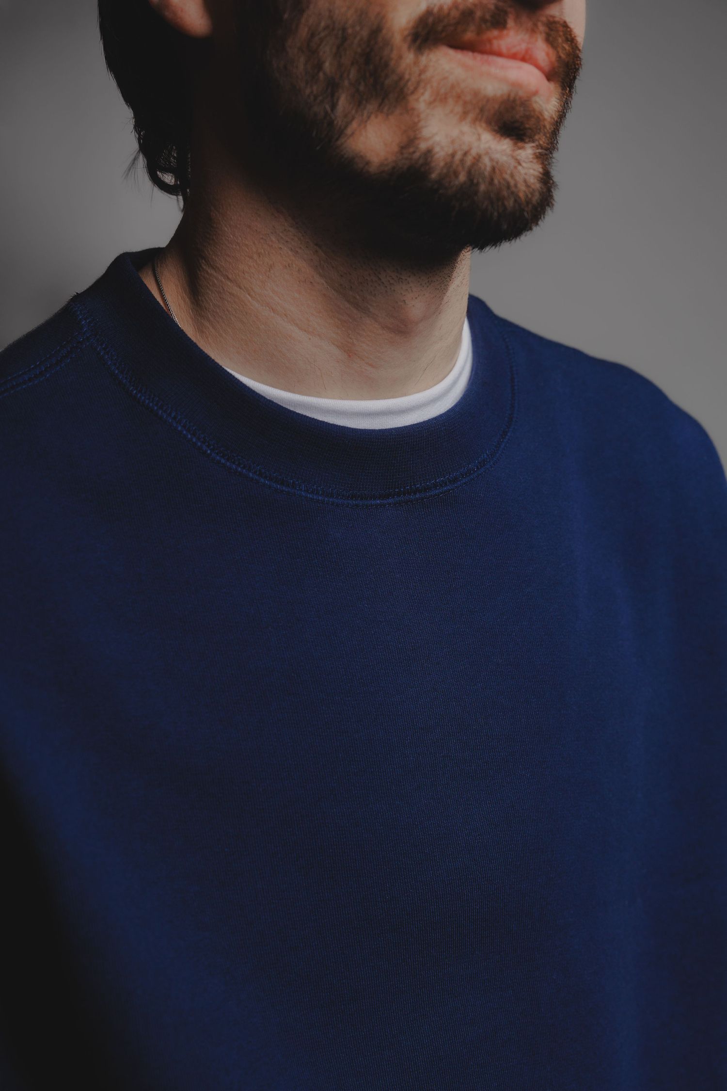 Close-up of man in navy blue crewneck sweatshirt with white undershirt and beard.