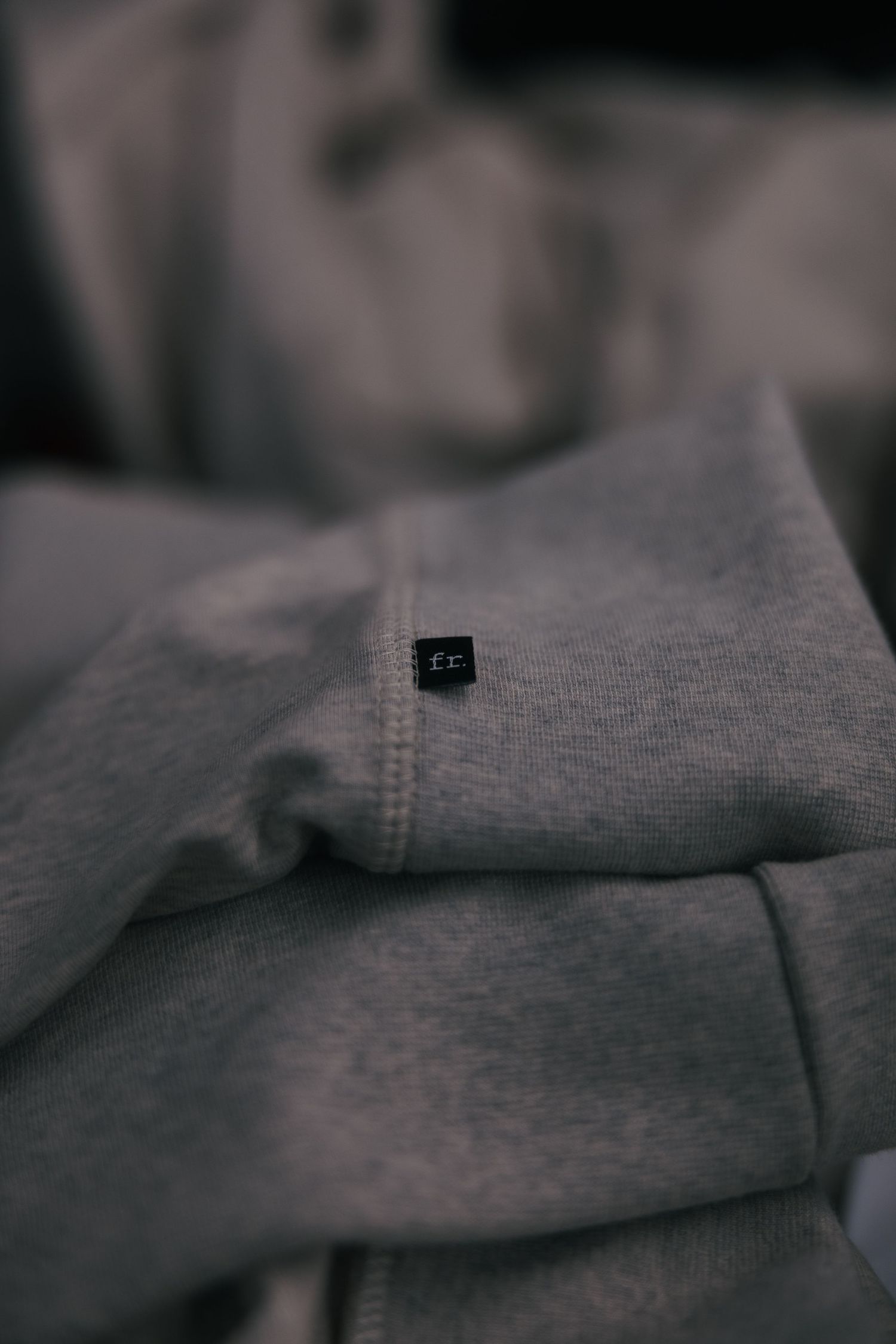 Close-up of a folded gray heather sweatshirt with a small black woven label on the sleeve.