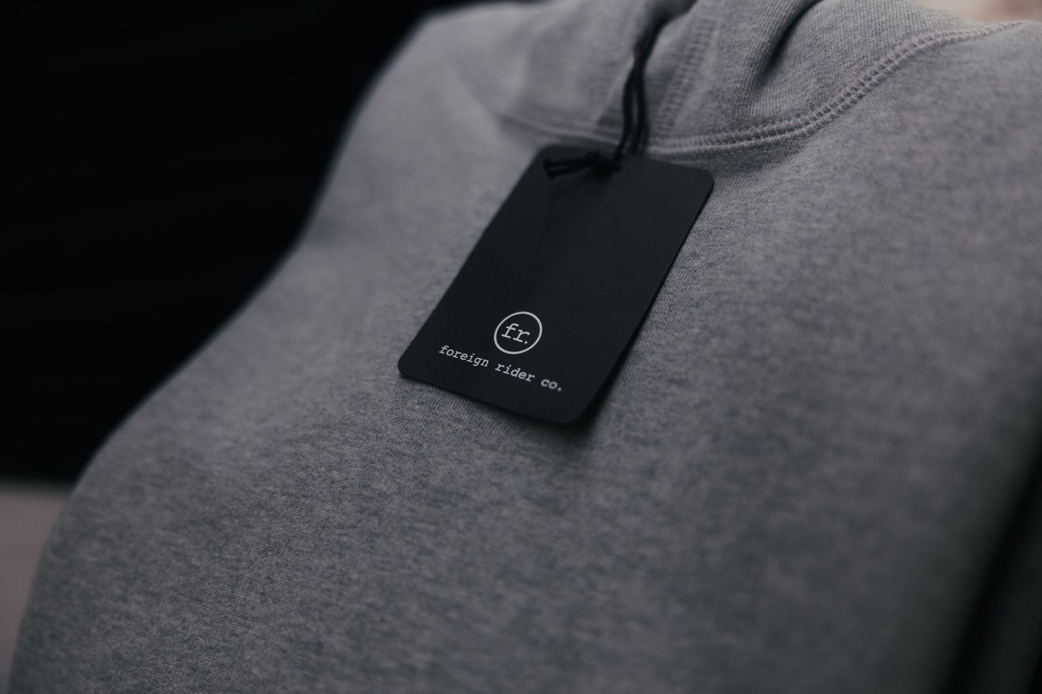 Gray hoodie with a black hang tag featuring a minimalist logo, showcasing premium clothing branding detail.