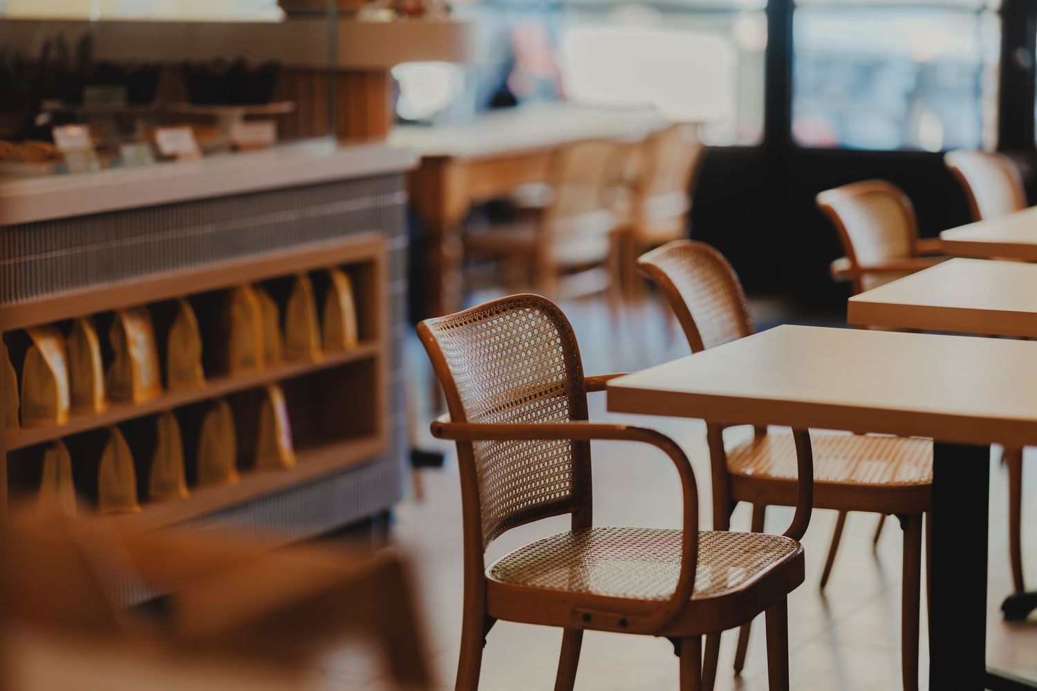 Cozy cafe interior with wooden rattan chairs, white tables, and a wooden shelf displaying bread loaves.