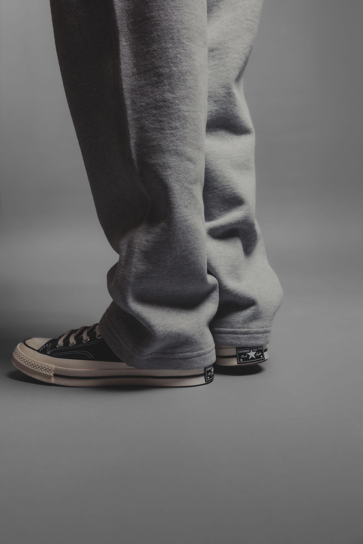 Grey sweatpants paired with black Converse Chuck Taylor sneakers on a neutral grey background.