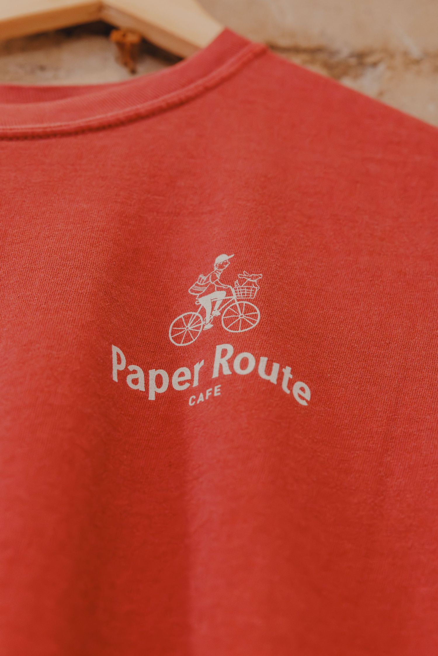 Red crewneck sweatshirt with Paper Route Cafe logo featuring a cyclist graphic printed in white.