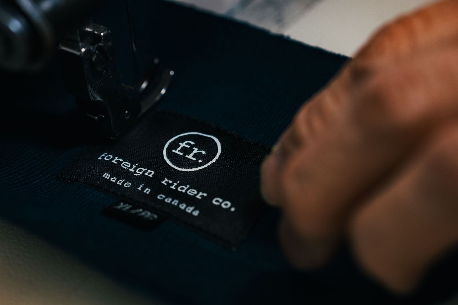 Close-up of a Foreign Rider Co. made in Canada label being sewn onto dark blue fabric.