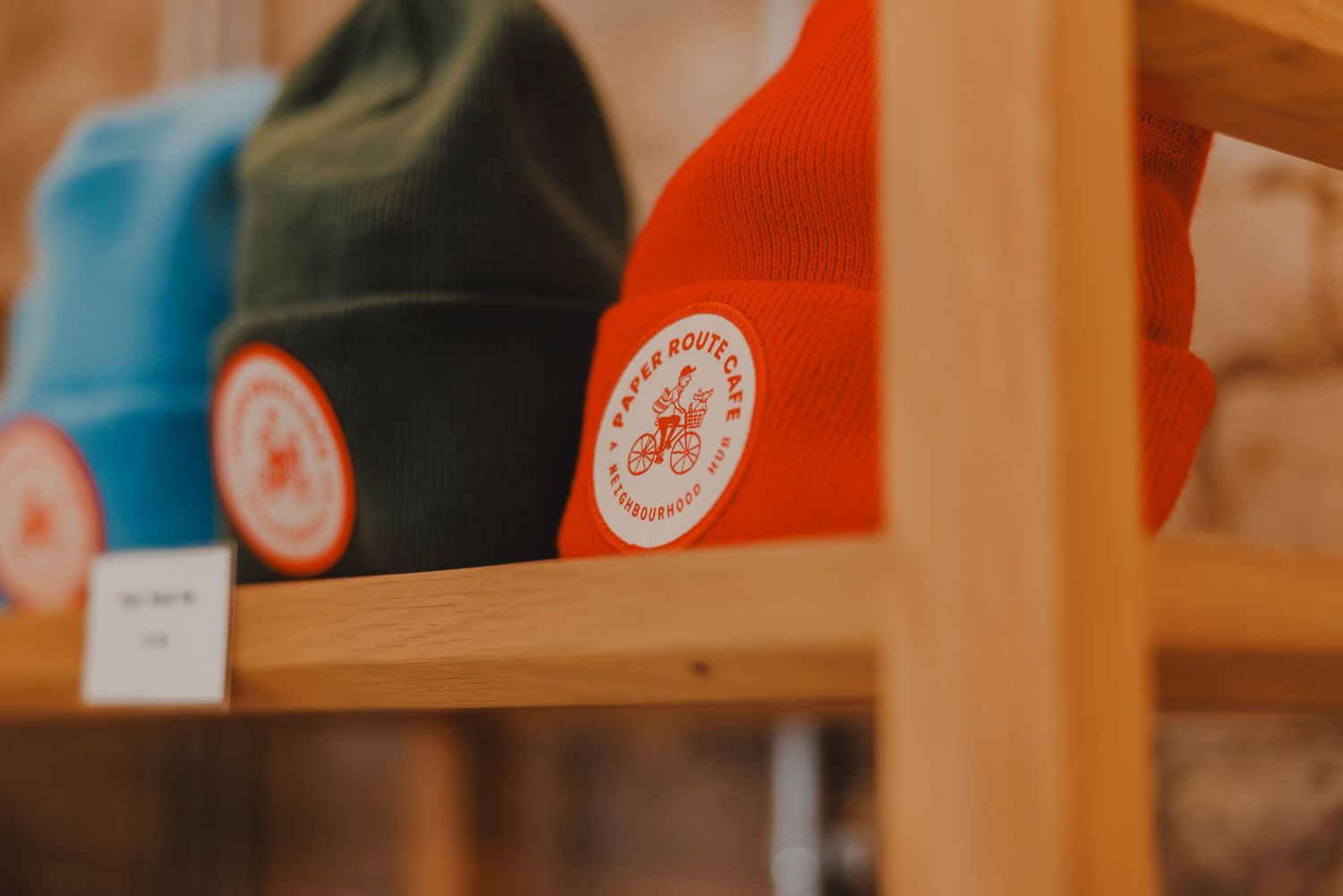 Colorful beanies displayed on wooden shelves featuring an orange circular logo patch in a retail store.