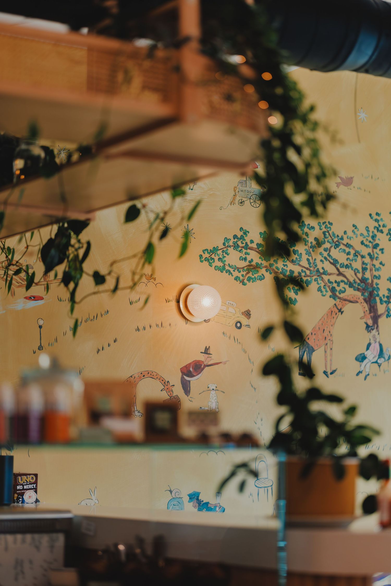 Whimsical cafe wall mural with animals and plants, illuminated by warm vintage light bulb.