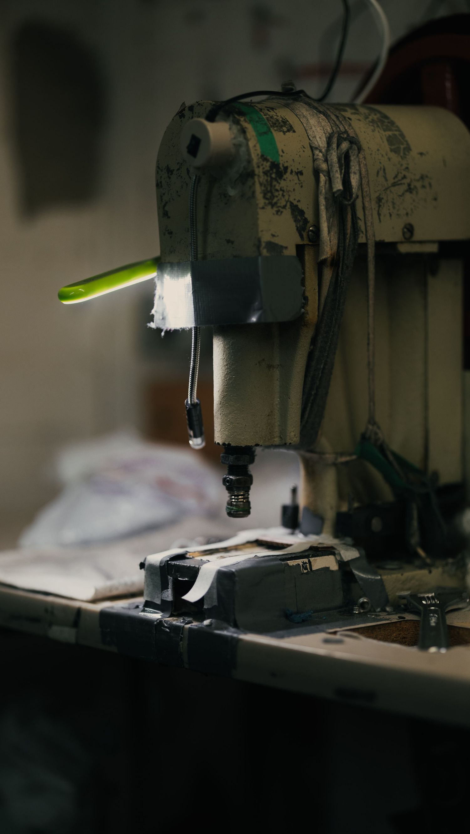 Aged industrial sewing machine with worn paint on a cluttered workbench in a dimly lit workshop.