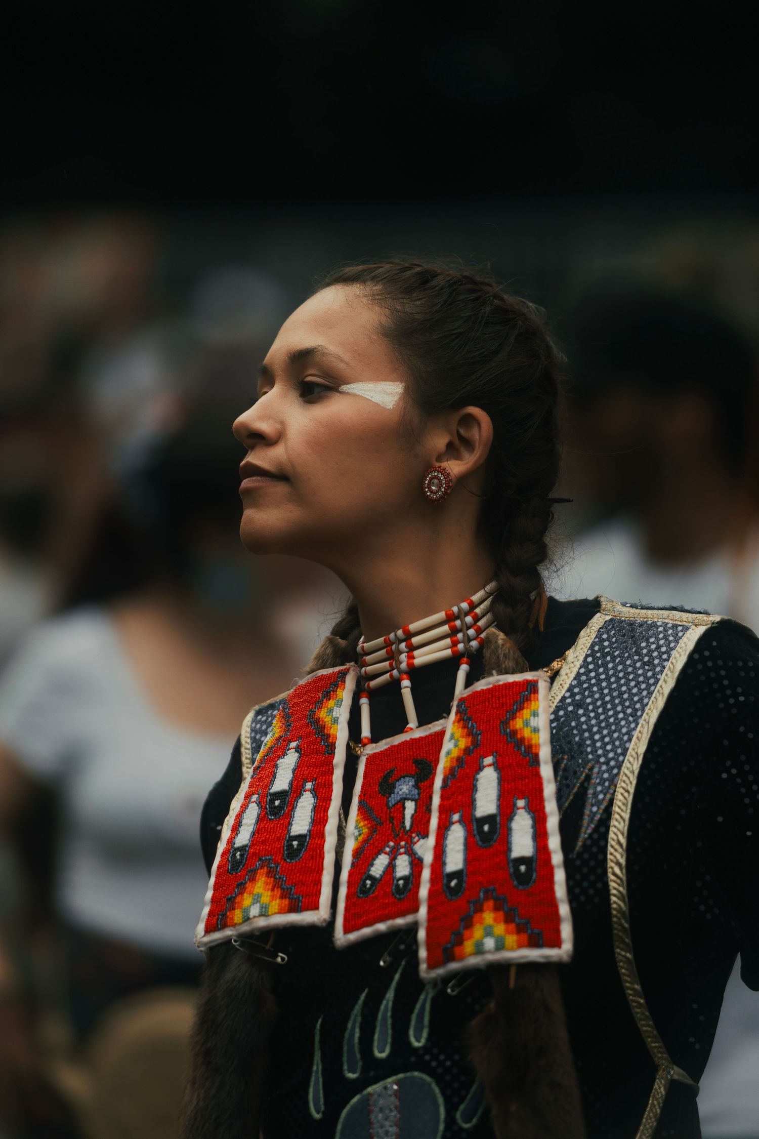 Young Native American woman in traditional beaded regalia with braided hair at a powwow celebration.