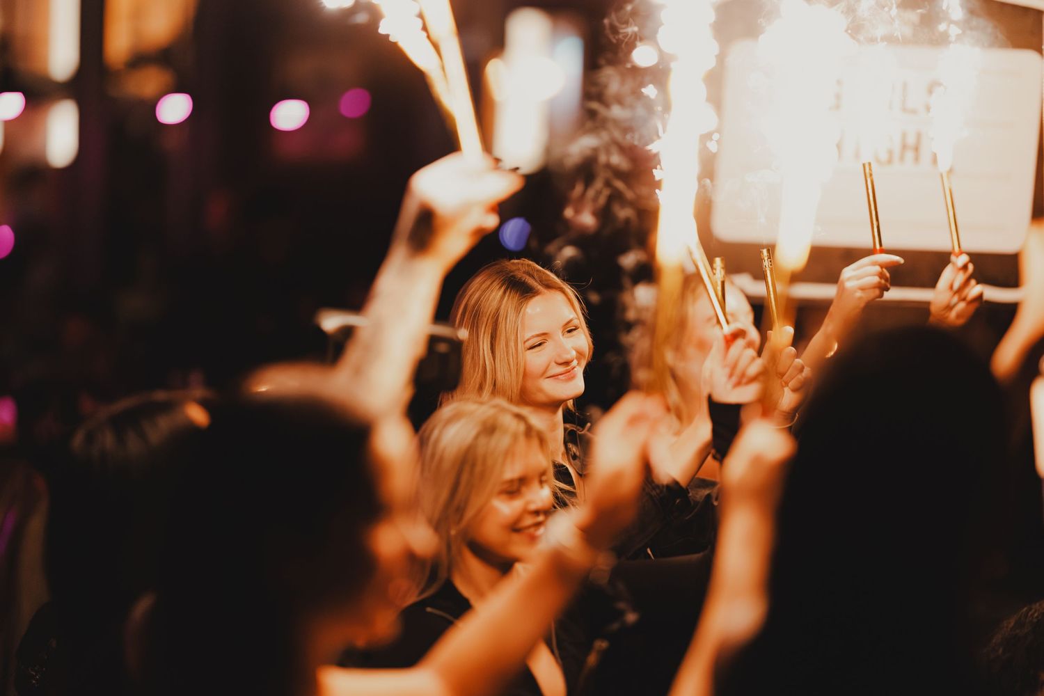 Joyful woman smiling at a festive night celebration surrounded by guests holding sparklers.
