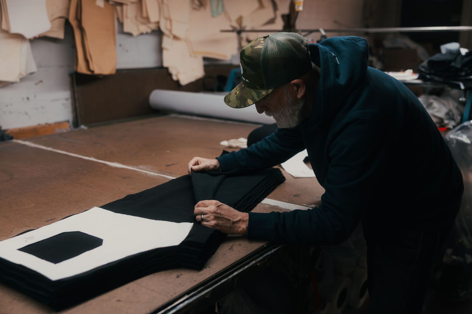 A craftsman carefully works on cutting black fabric pieces on a workbench in a leather goods workshop.