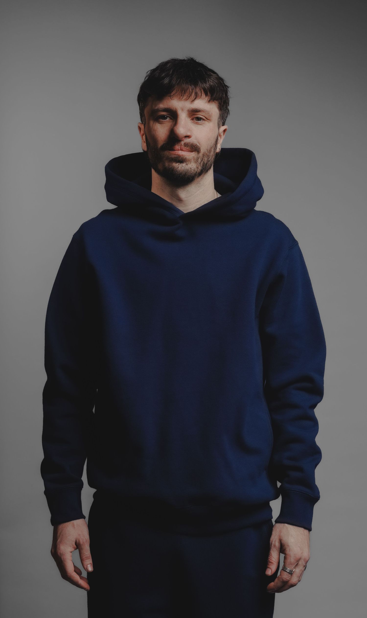 Man wearing navy blue oversized hoodie standing against grey studio background.