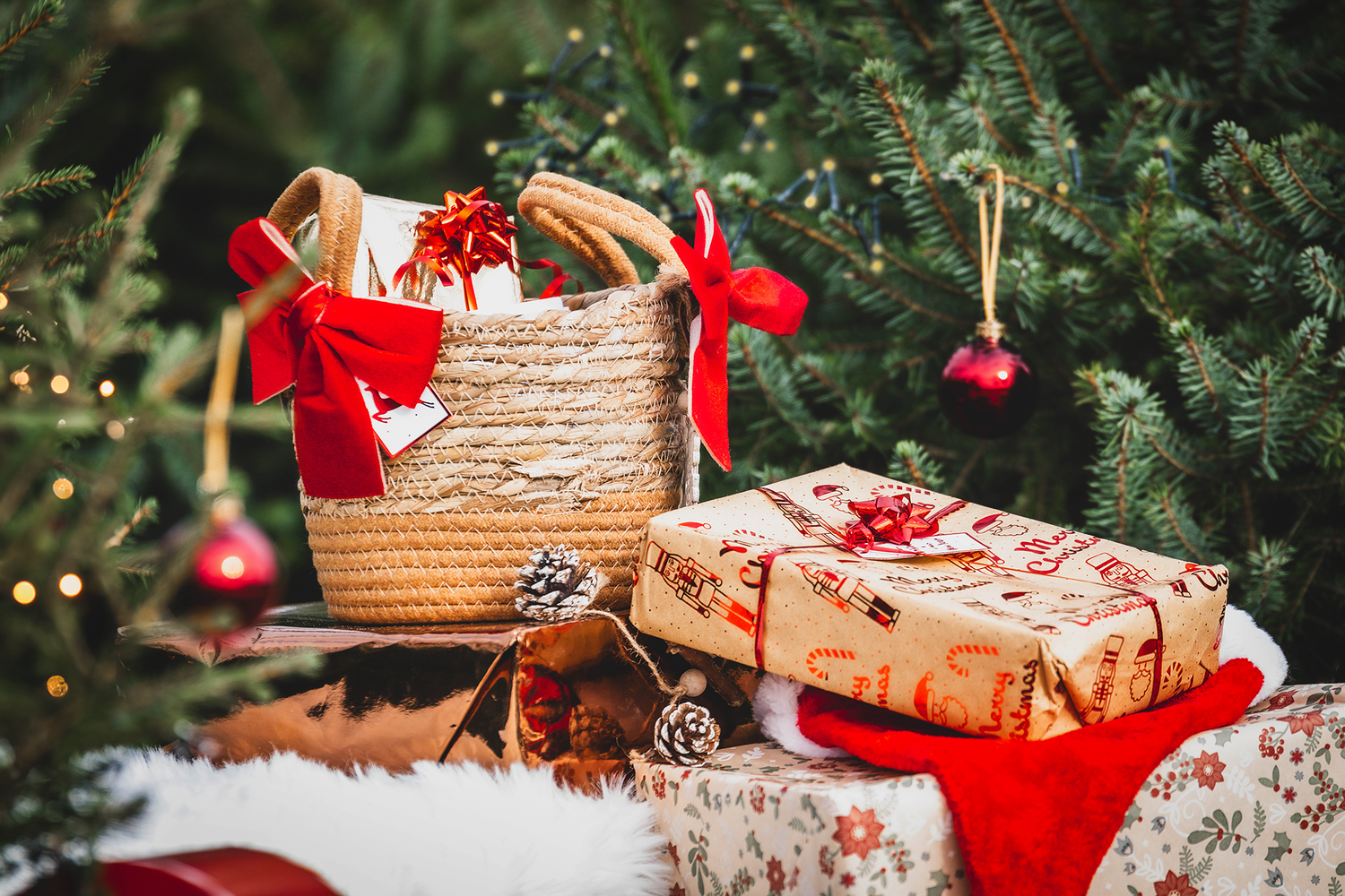 Festive Christmas gifts with red bows arranged under decorated pine tree with ornaments.
