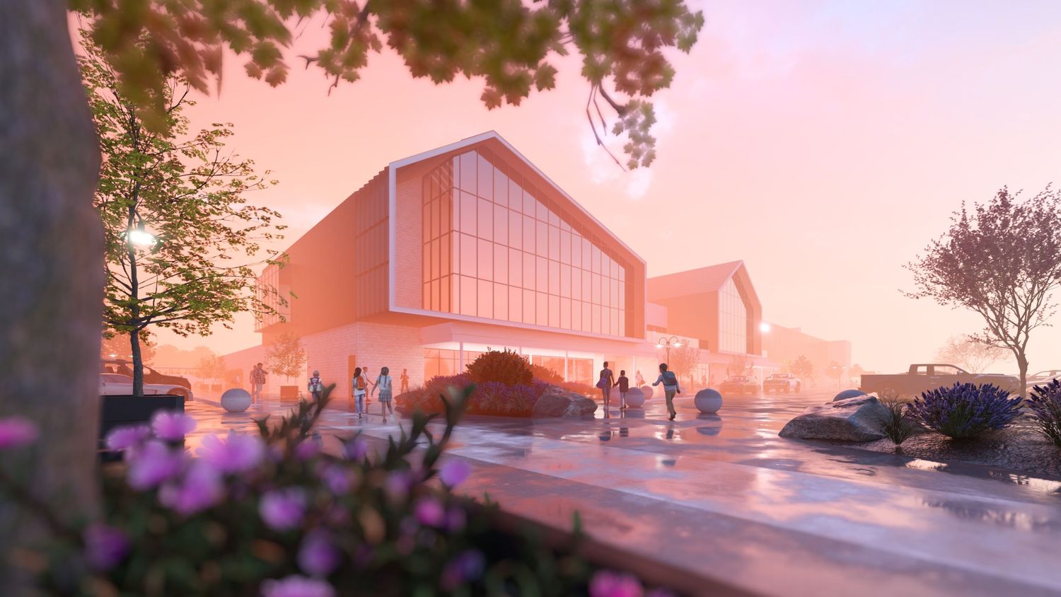 A pink sunset casts a warm glow over a modern glass building and parking lot with trees silhouetted against the sky.