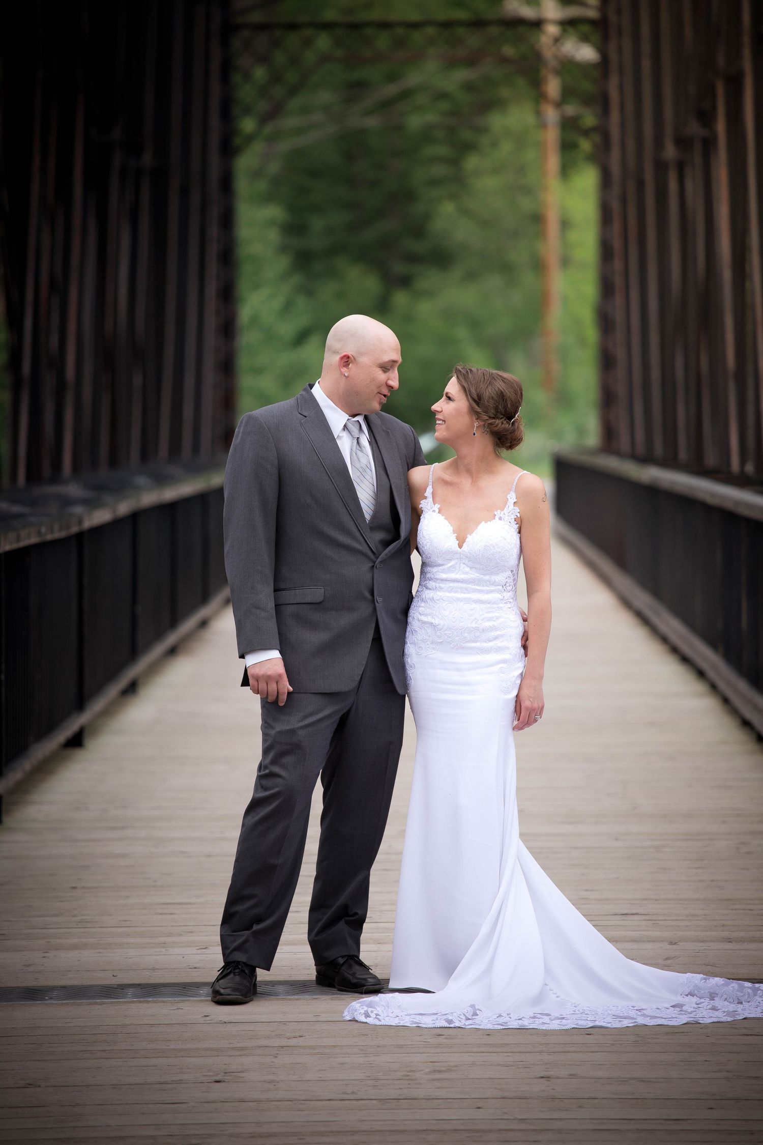Wedding couple posing together on a rustic wooden bridge surrounded by trees.