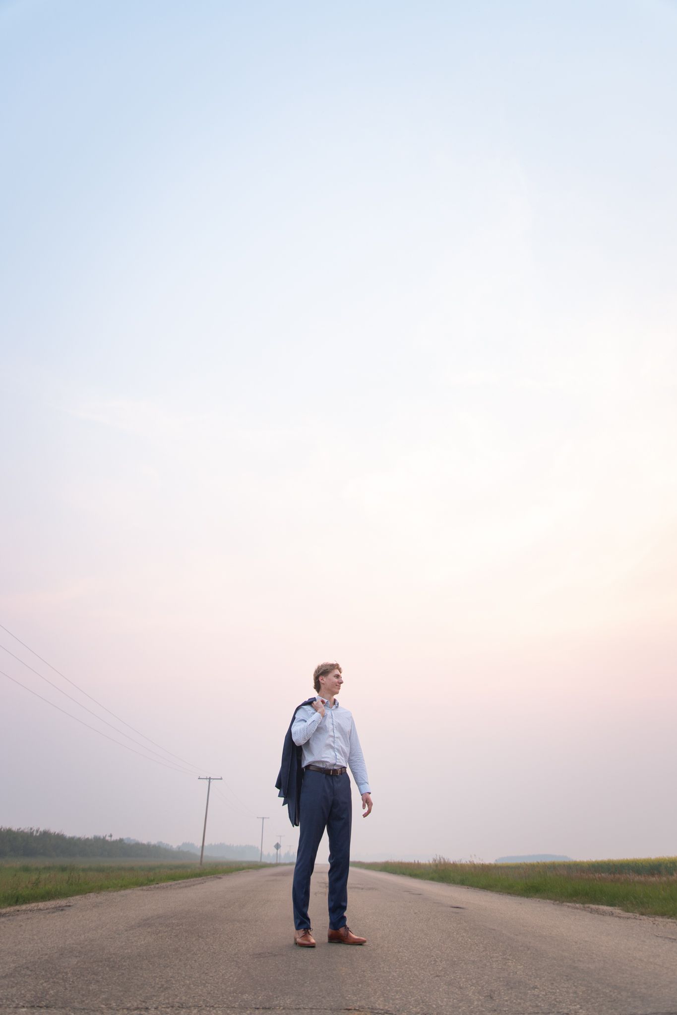 A person in business attire poses on an empty country road at sunset.