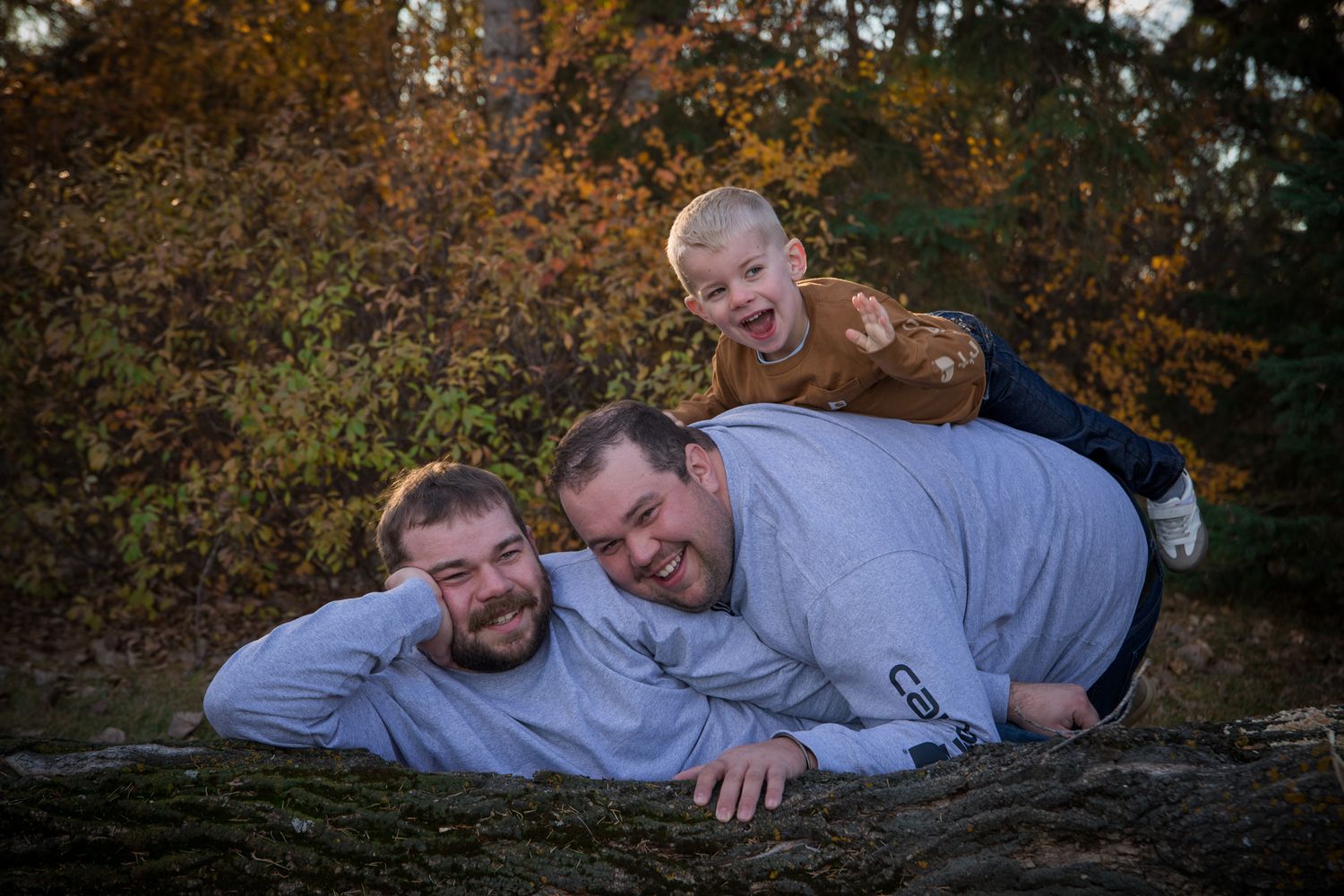 A relaxed family group lounging together on fallen logs in a natural outdoor setting.