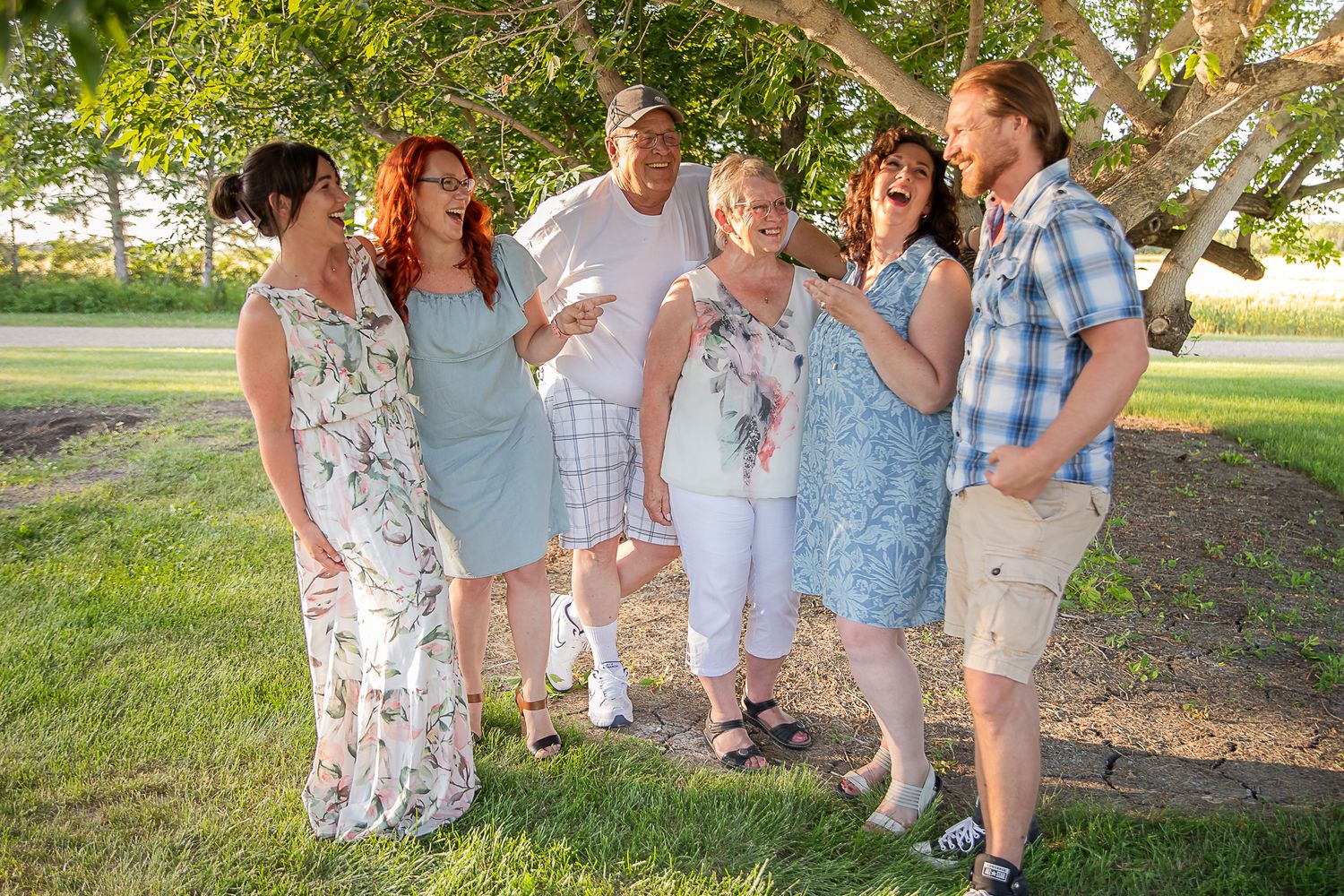 Extended family group photo in casual attire under trees on a sunny day.